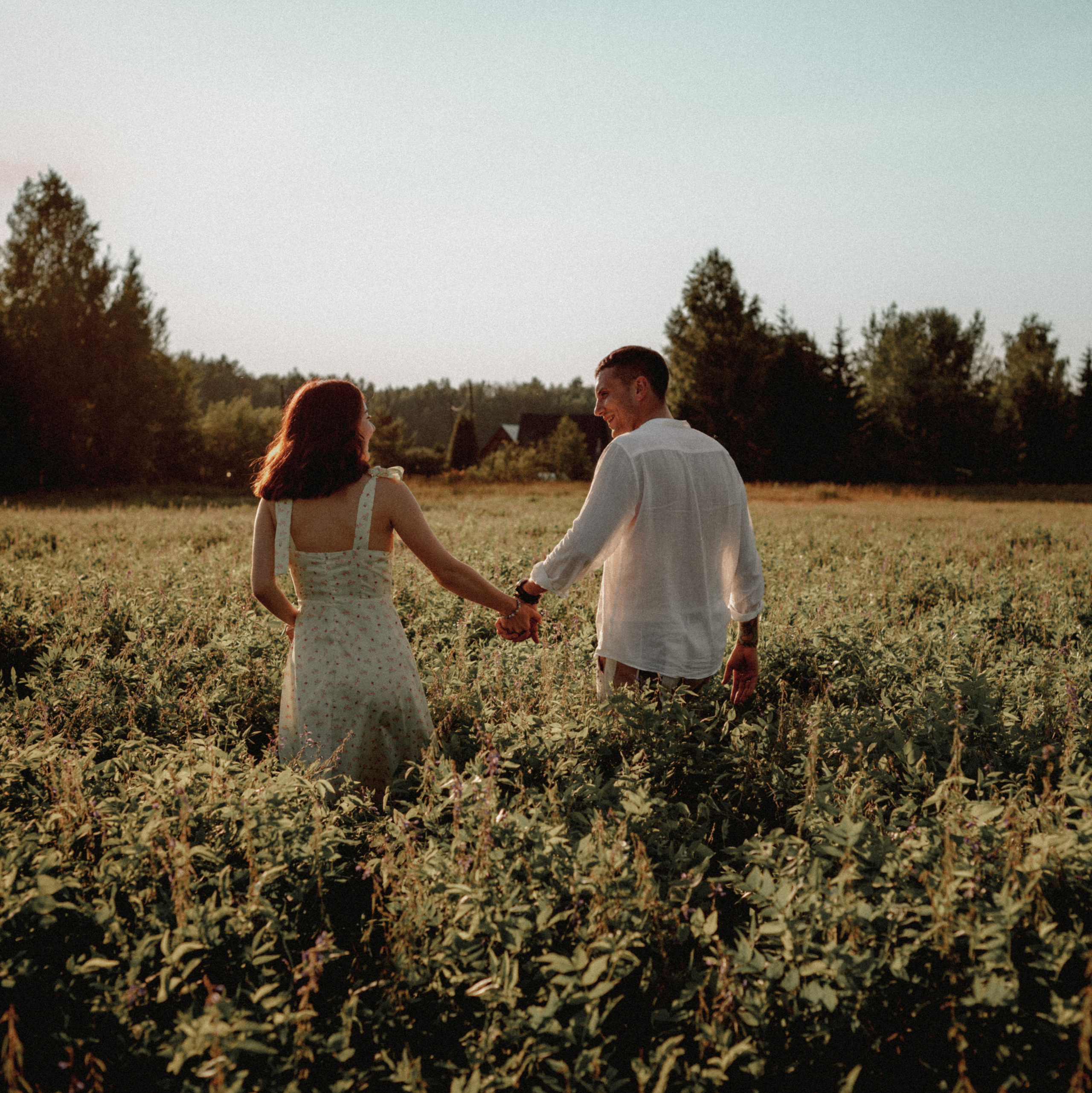 молодая пара на закате держится за руки в поле