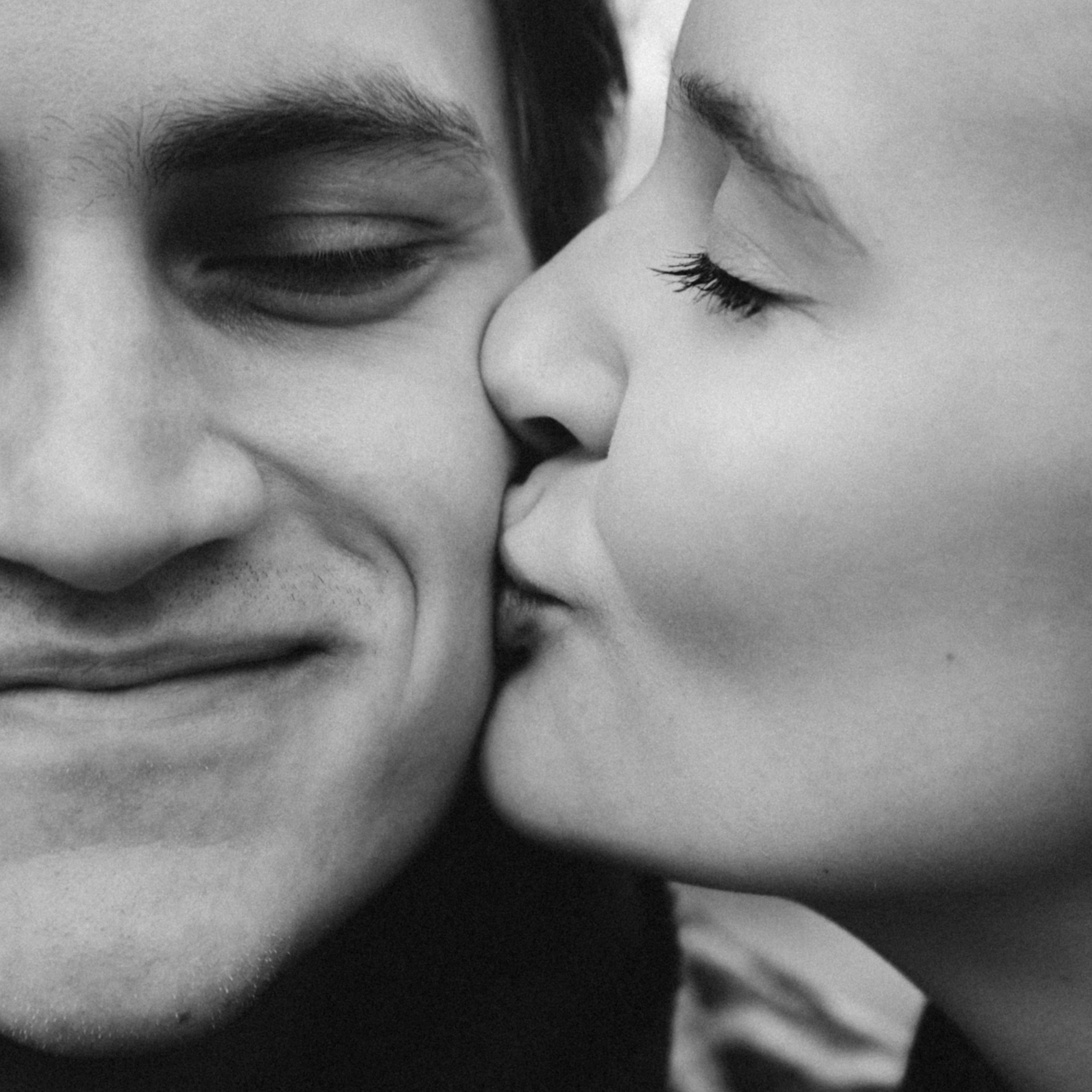 Черно-белое фото человека, целующего другого в щеку с нежностью, показывающее момент радости и ласки.