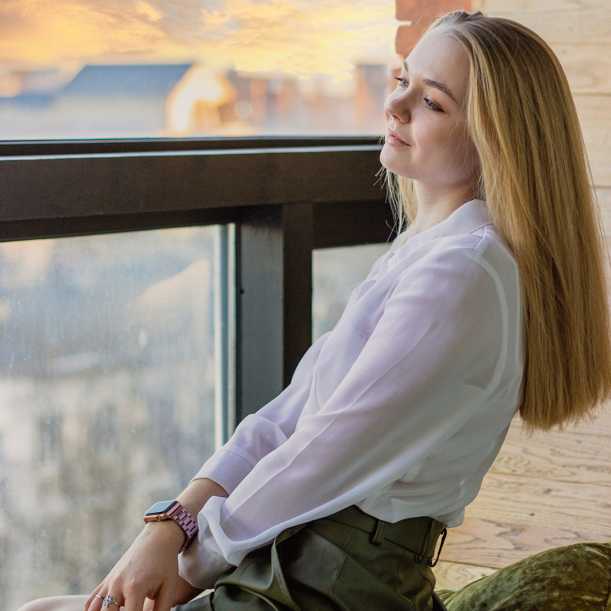 Девушка сидит на подоконнике и смотрит на закат