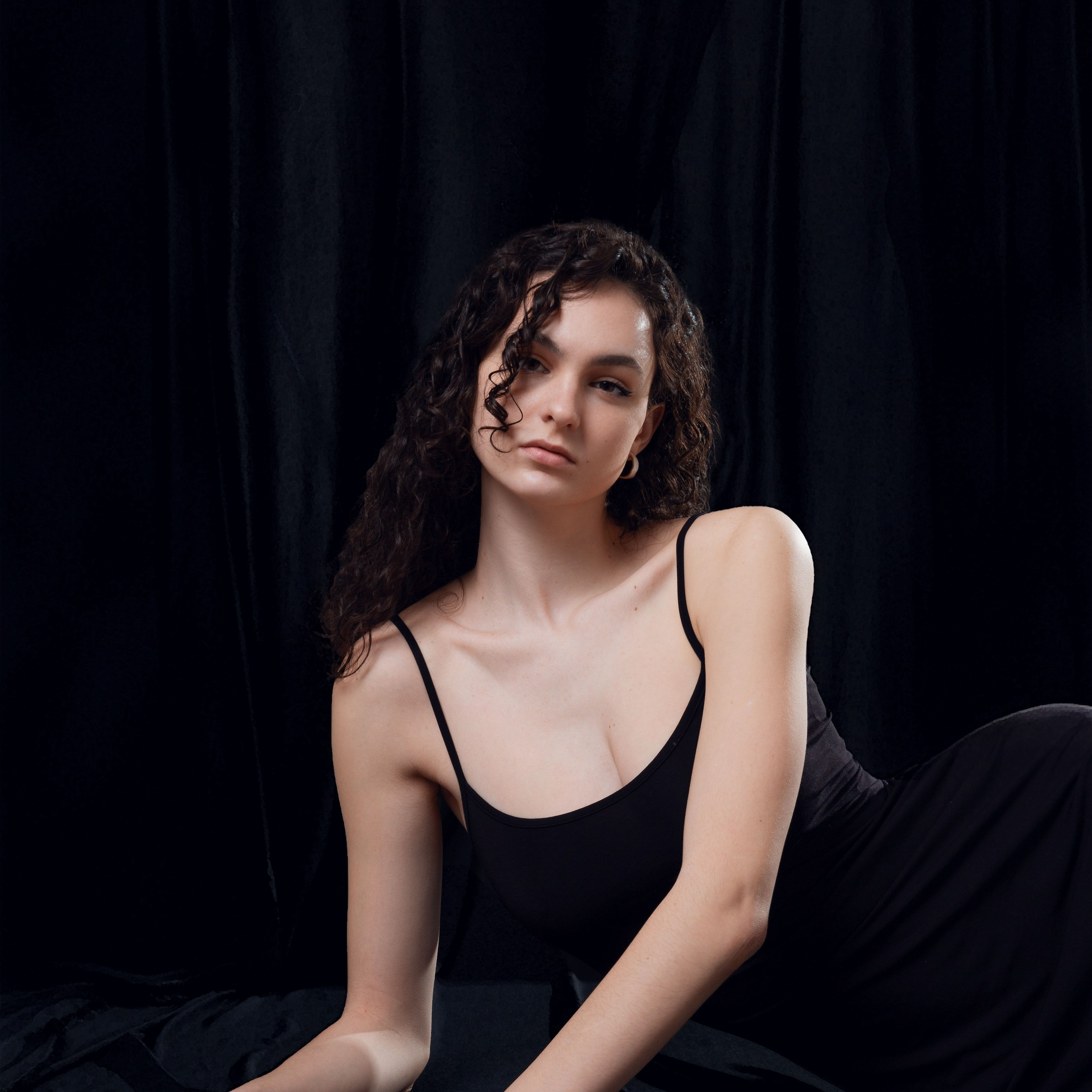 Девушка в чёрном платье сидит на полу на тёмном фоне. Портрет для иллюстрации стоимости фотосессии.