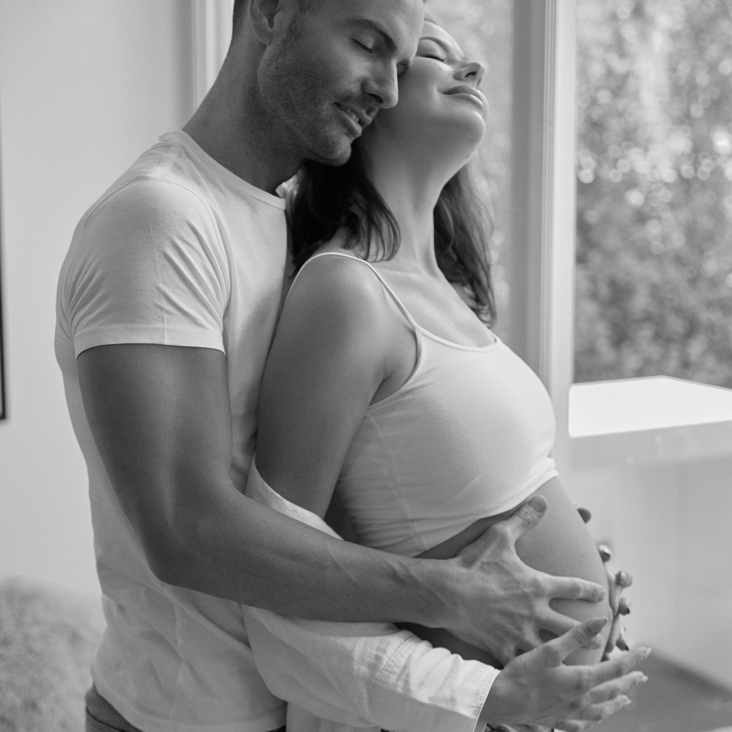 Couple embracing by the window, capturing a tender moment of their maternity journey with the best maternity photo in Emirates