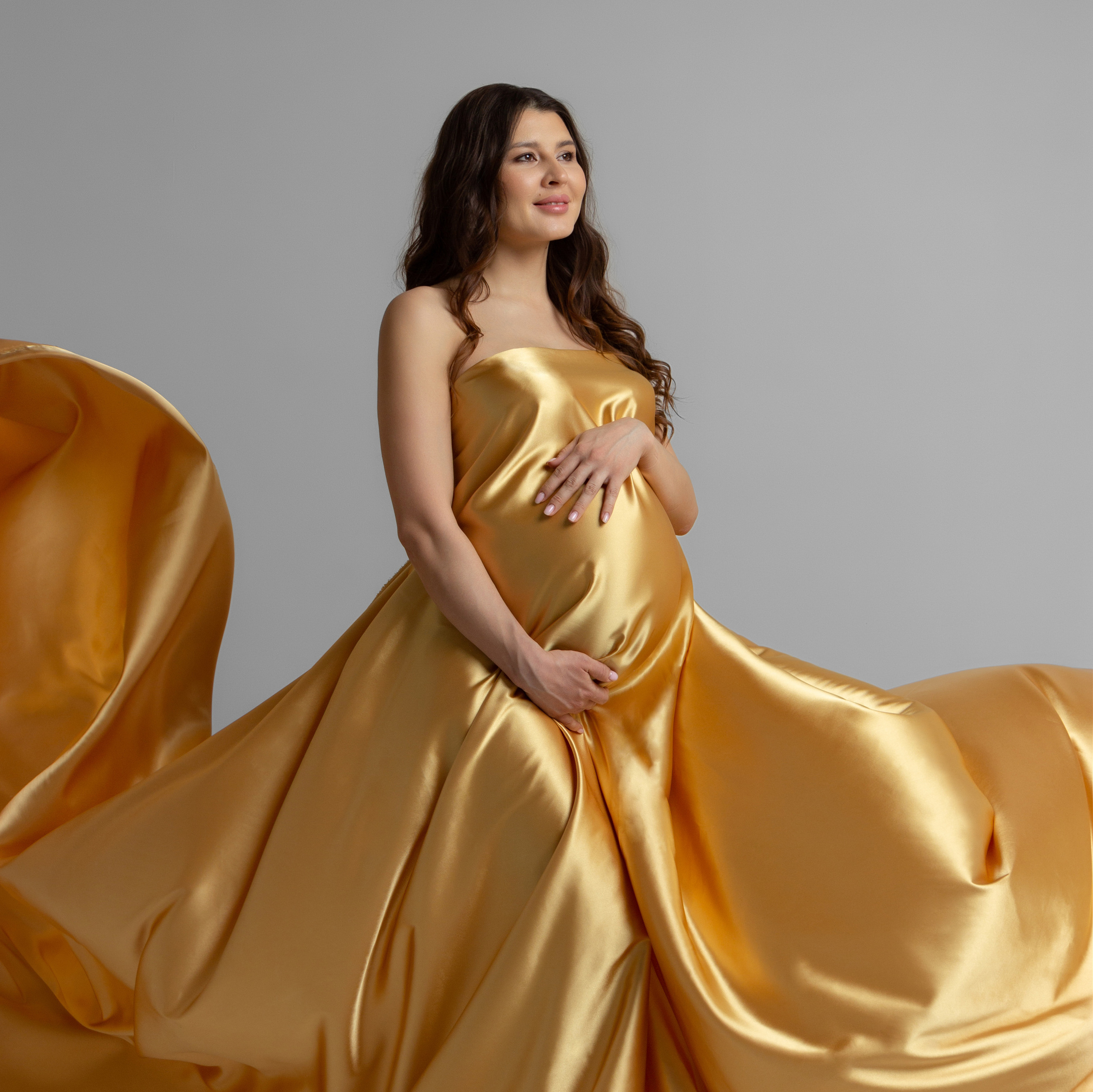 беременная девушка в золотой развивающейся ткани