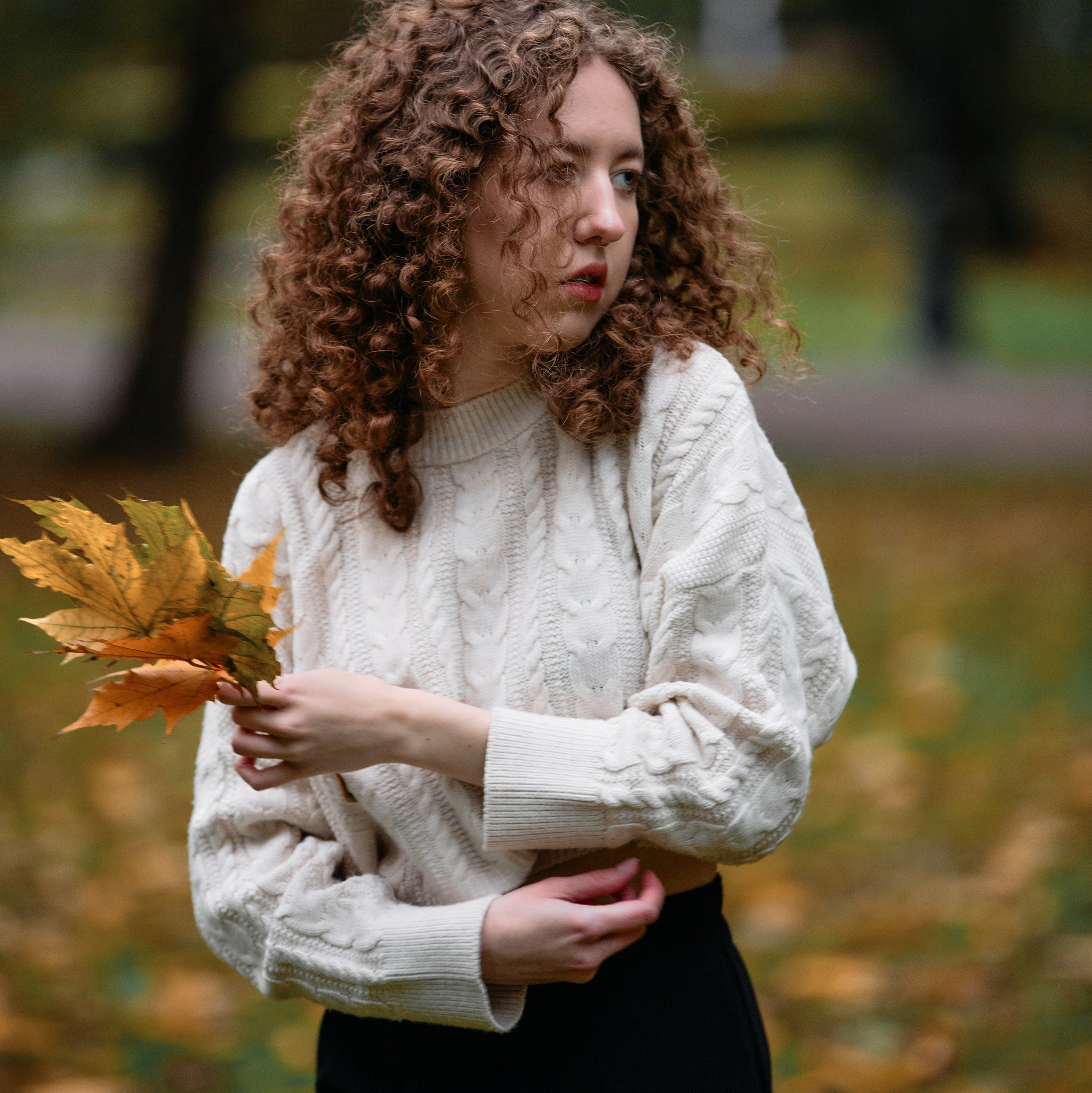 Осенняя фотосессия на улице: девушка в белом свитере и джинсах среди листвы.