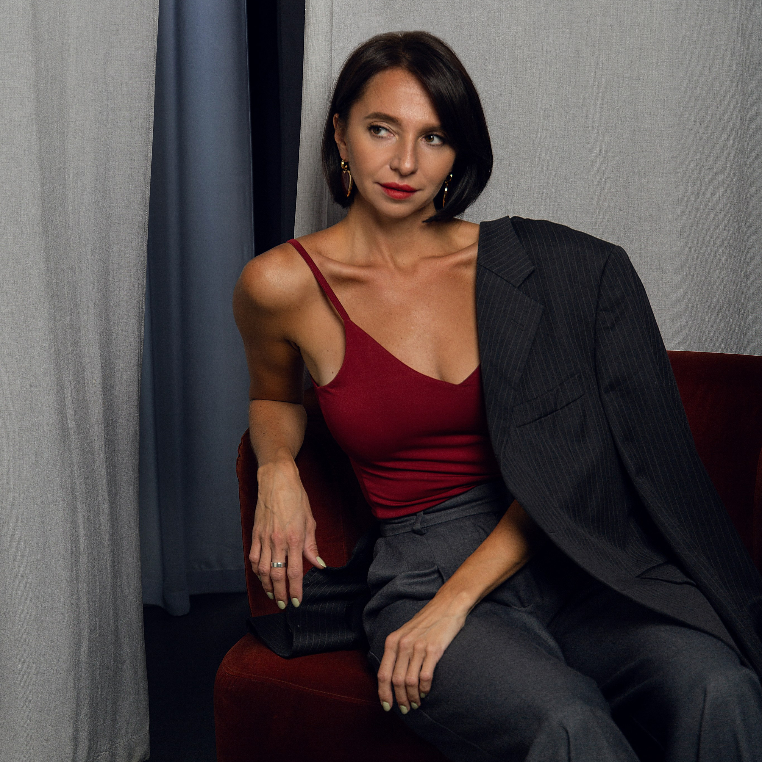 Элегантная фотосессия в студии: девушка в красном платье на фоне серых стен.