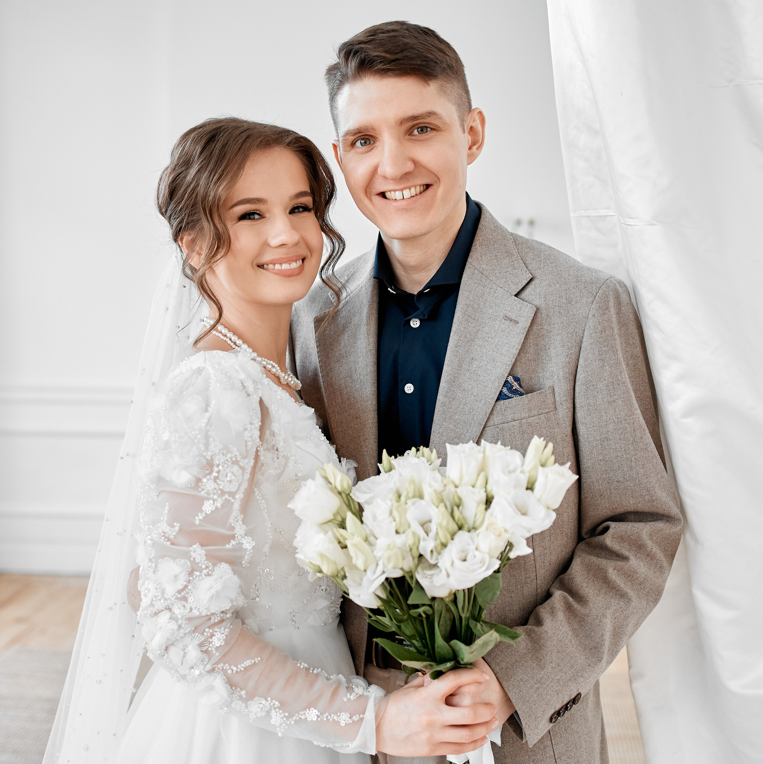 Невеста и жених улыбаются, держа букет.