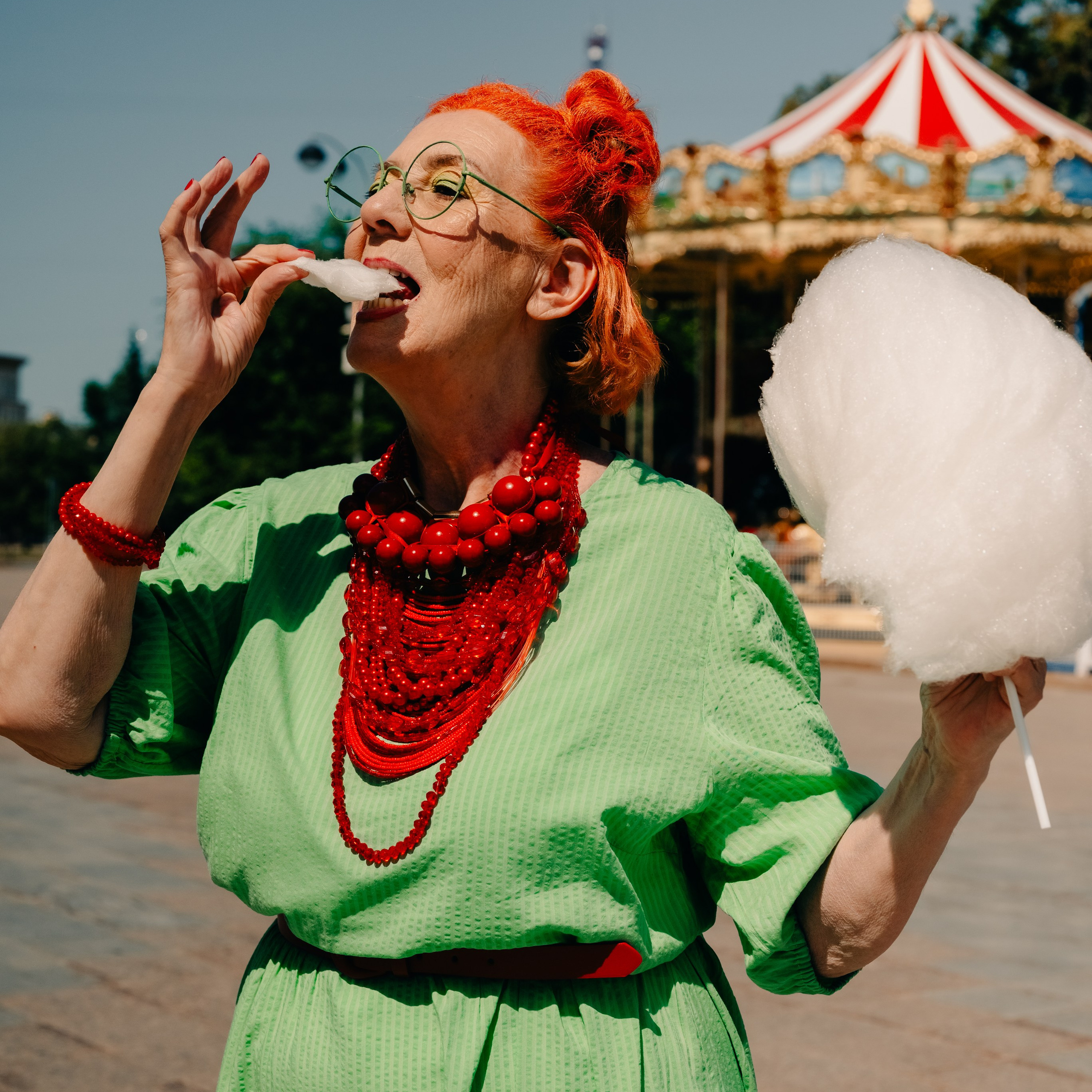 бабушка ест сладкую вату в парке аттракционов