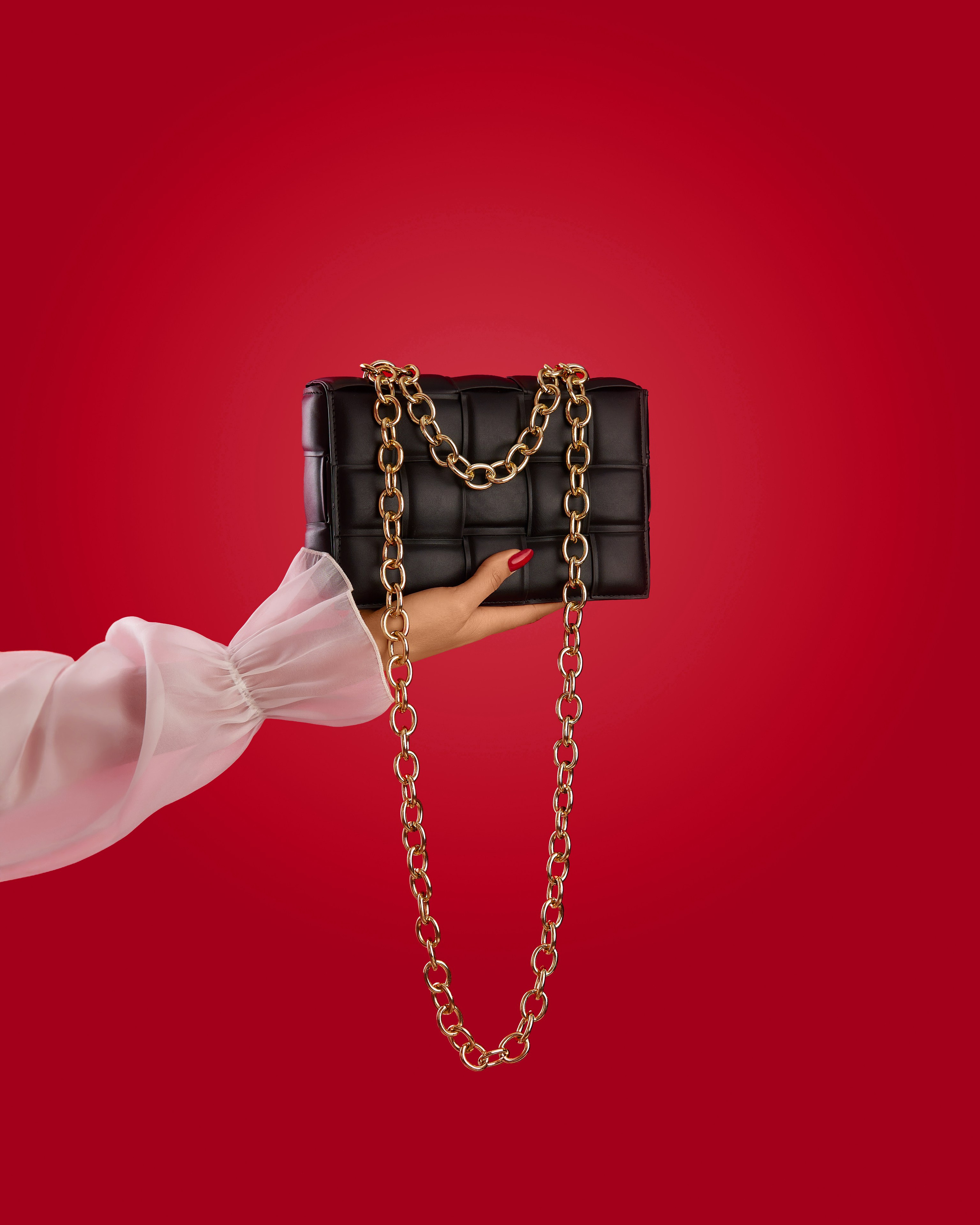 Рука девушки модели держит черную сумку на красном фоне