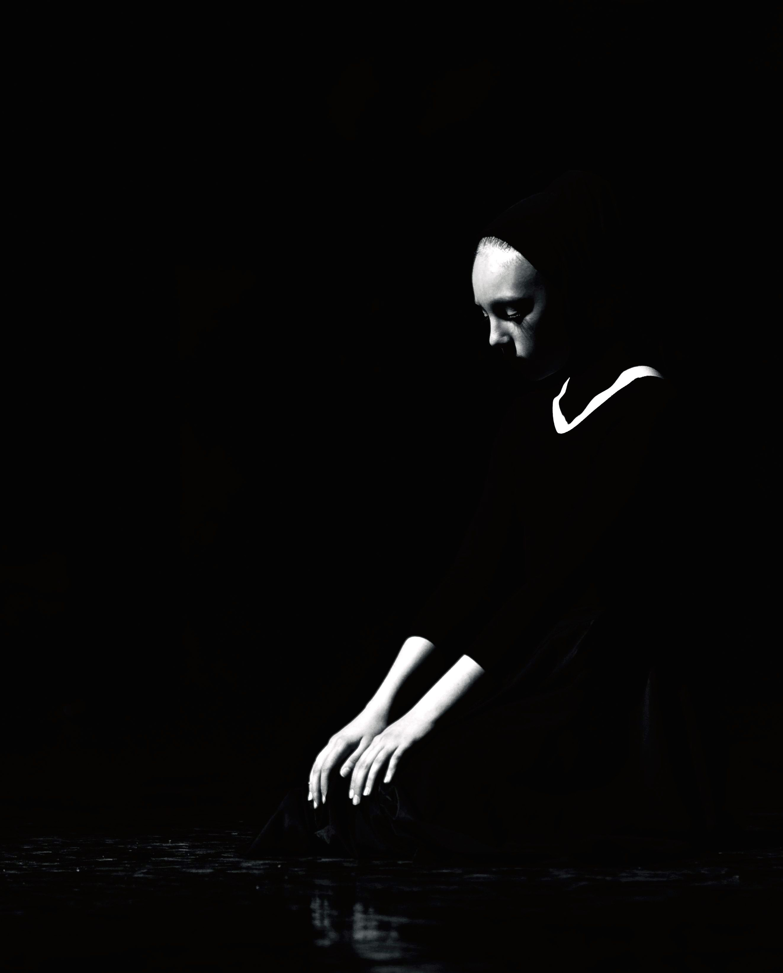 Одиночная фигура в черном в темноте с контровым светом на лице и руках, минималистичная композиция, медитативное состояние