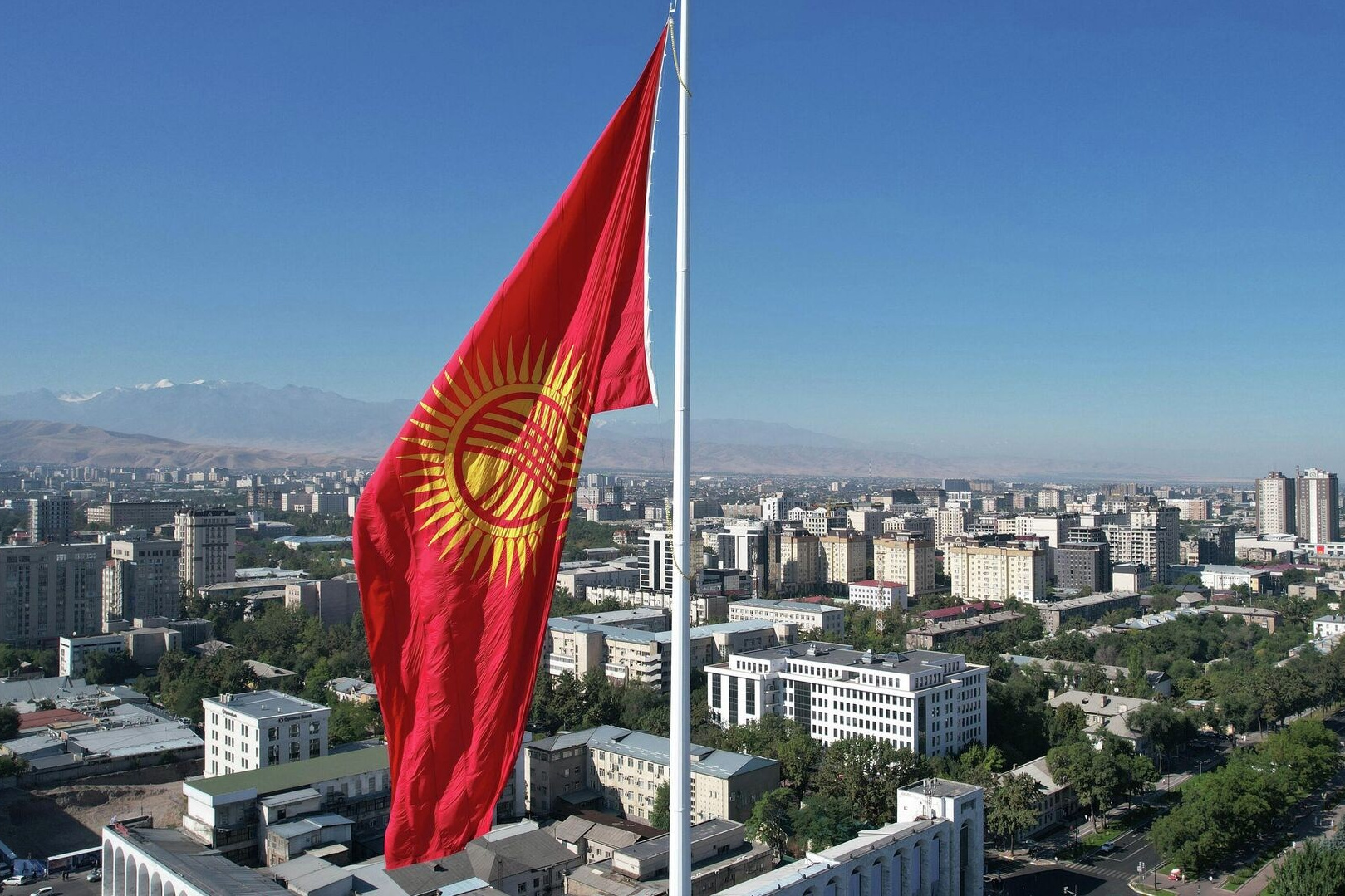 Горное озеро Иссык в Алматинской области, Казахстан, с бирюзовой водой на фоне осеннего леса с яркими золотистыми деревьями, окружённого высокими горами, покрытыми хвойным лесом. На горизонте видны заснеженные вершины под облачным небом