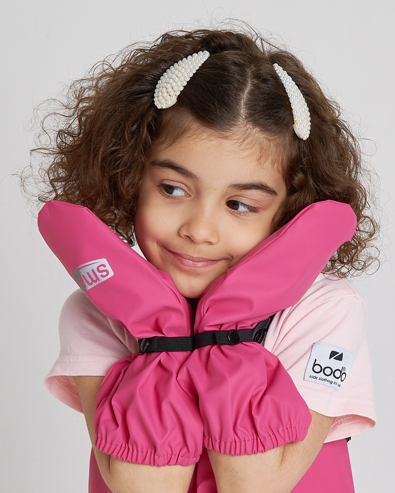 Девочка улыбается и держит лицо в руках с рукавицами