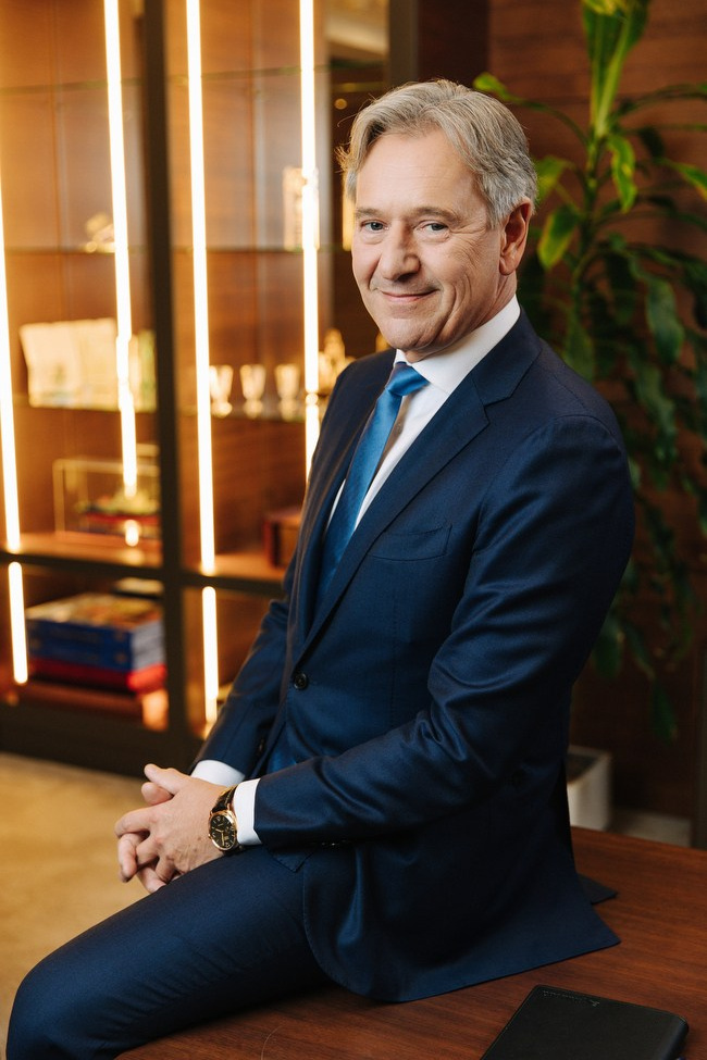 Корпоративный портрет топ-менеджера в рабочем кабинете — мужчина в синем костюме с красным галстуком на фоне стеллажа с грамотами, цветная деловая фотосессия