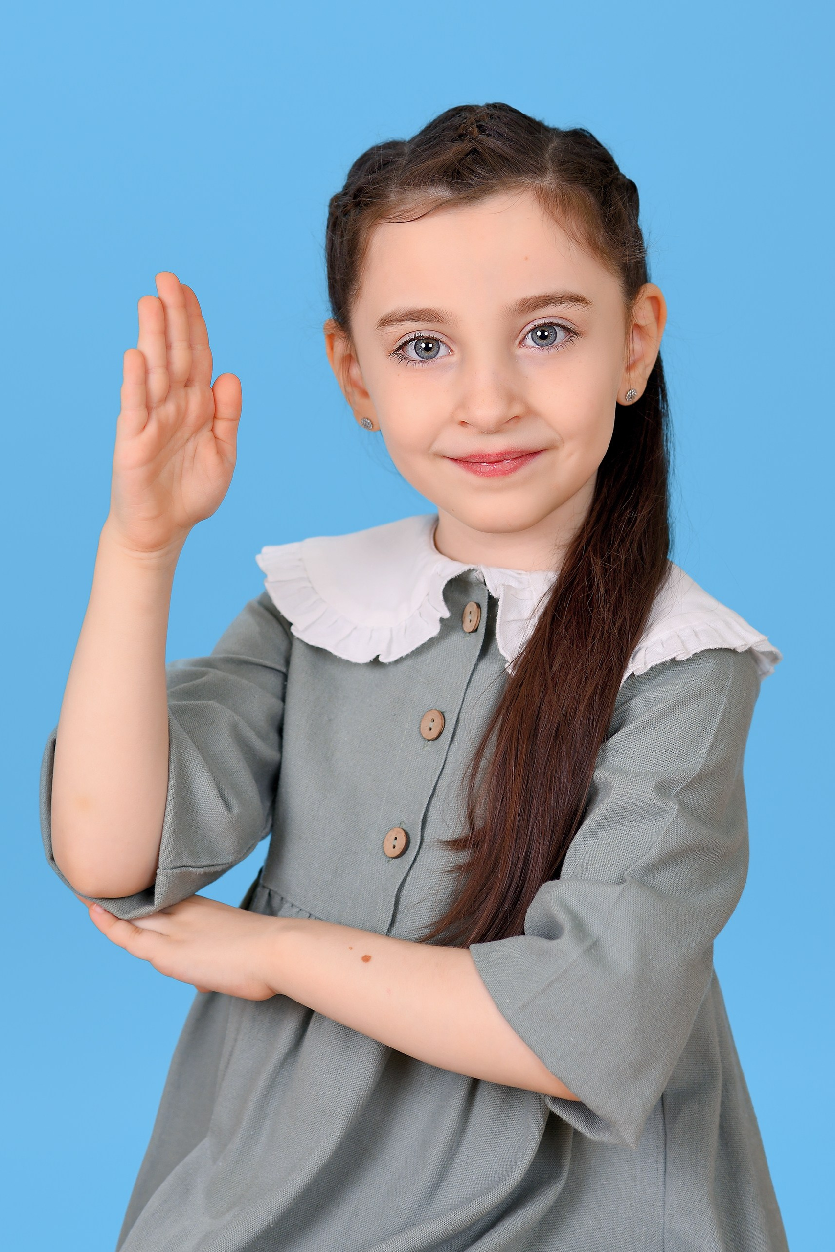 Портрет улыбающейся девочки в клетчатом платье, поднявшей руку вверх для ответа.