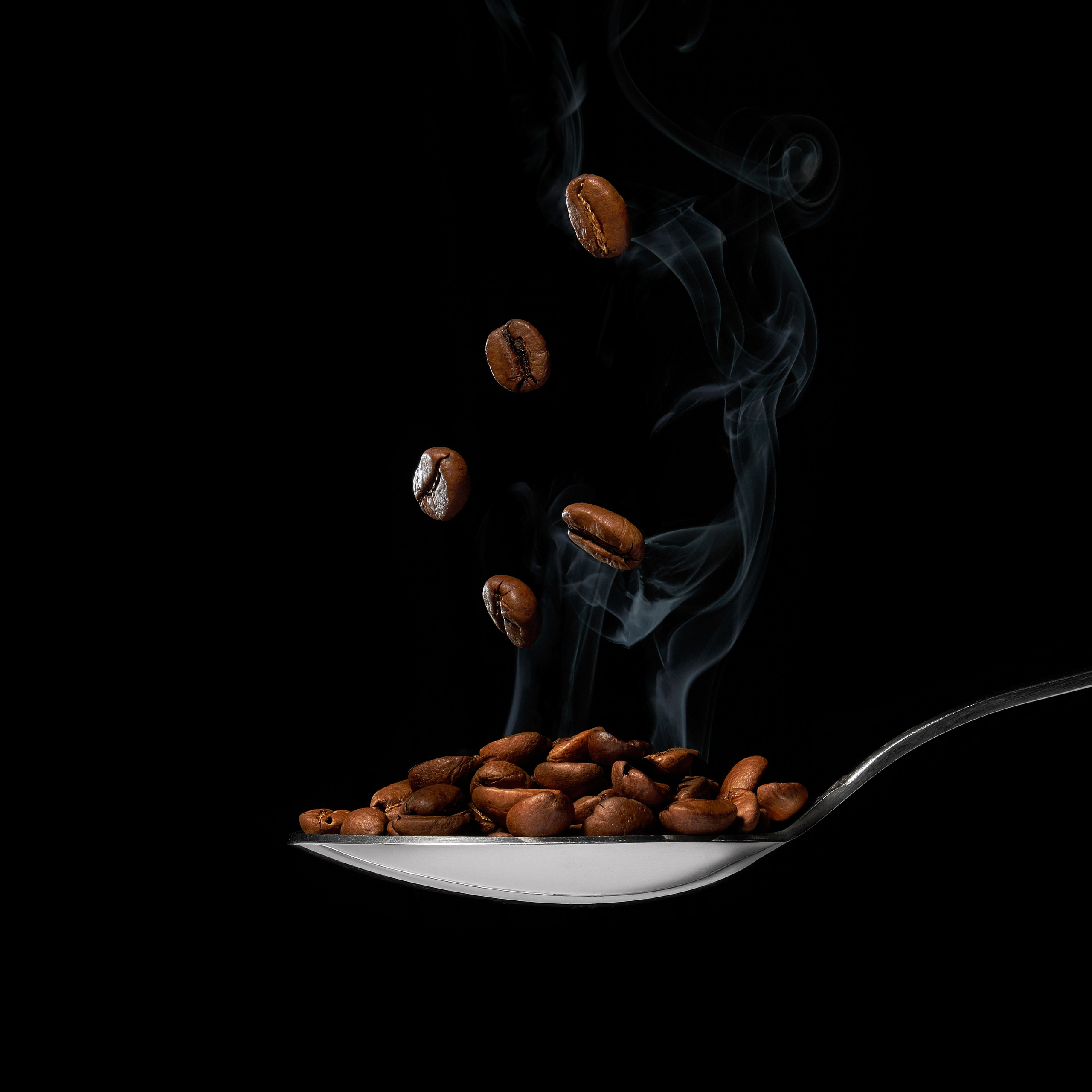 Зерна кофе в момент падения в металлическую ложку на тёмном фоне