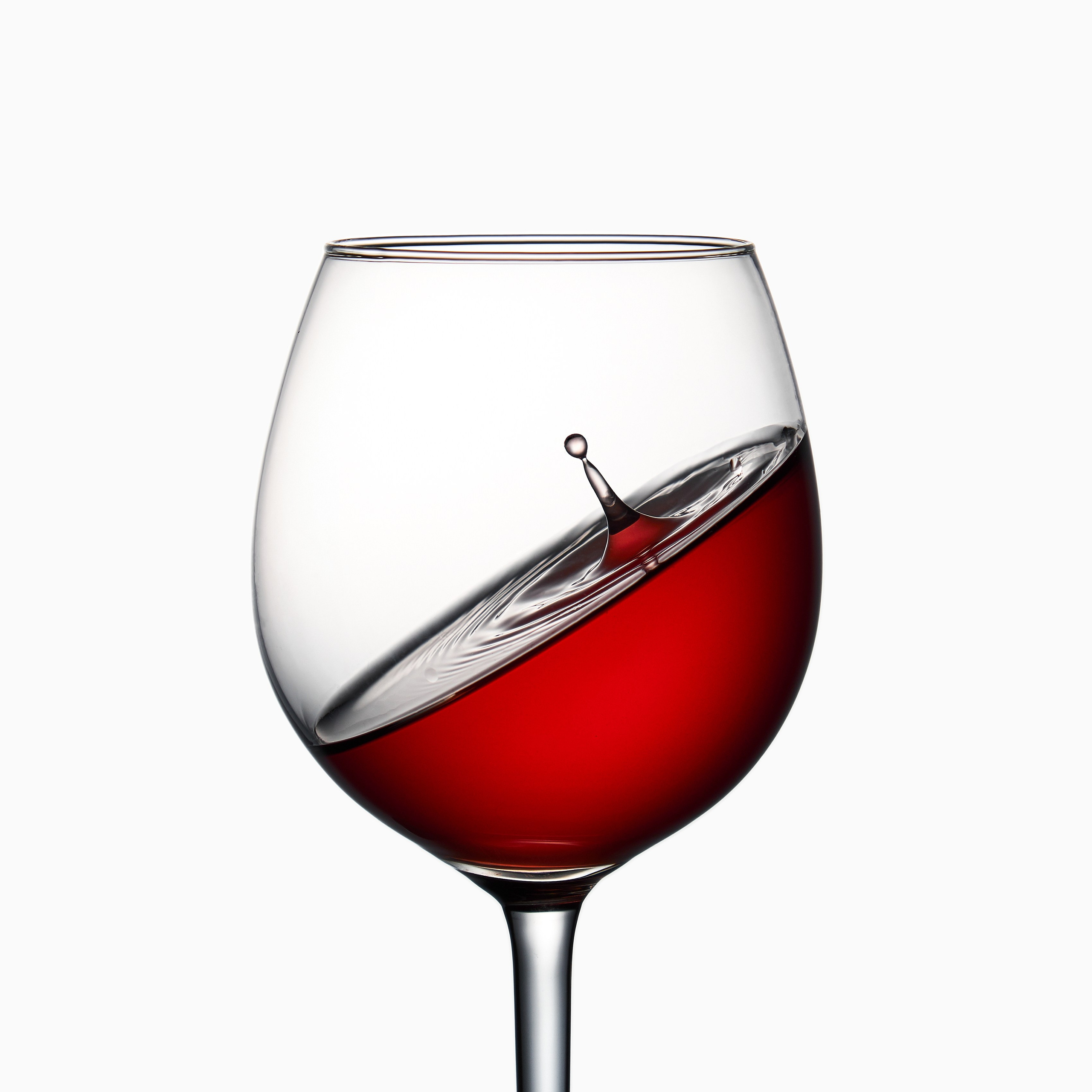 Бокал с красным вином и всплеском внутри, изолированный на светлом фоне, концептуальная предметная фотография