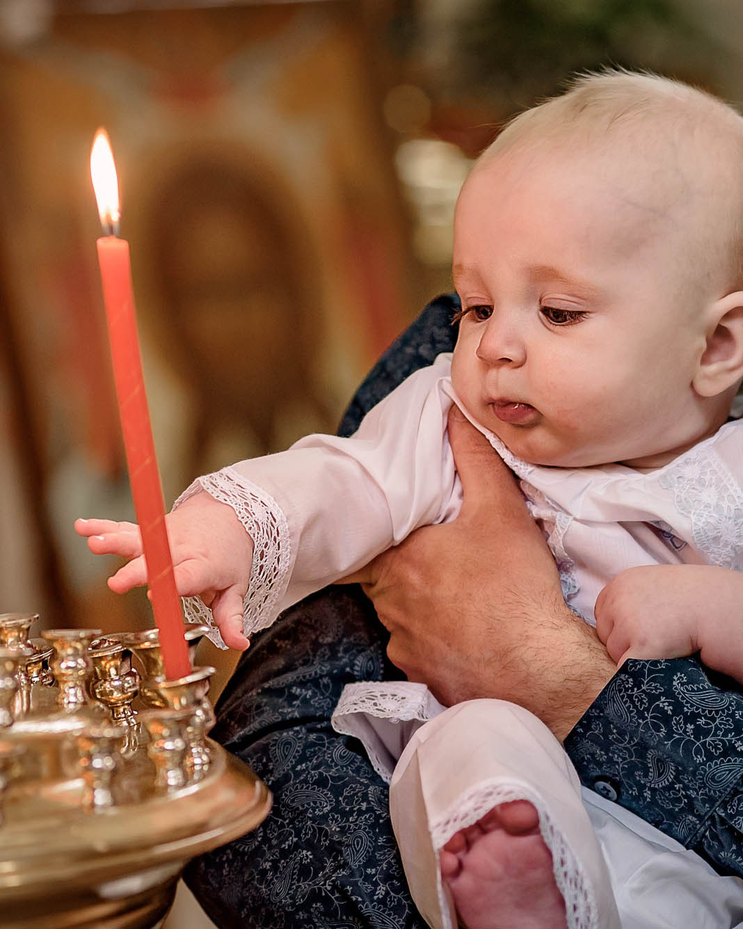 маленький ребенок на руках  у папы в церкви рядом с горящими свечами