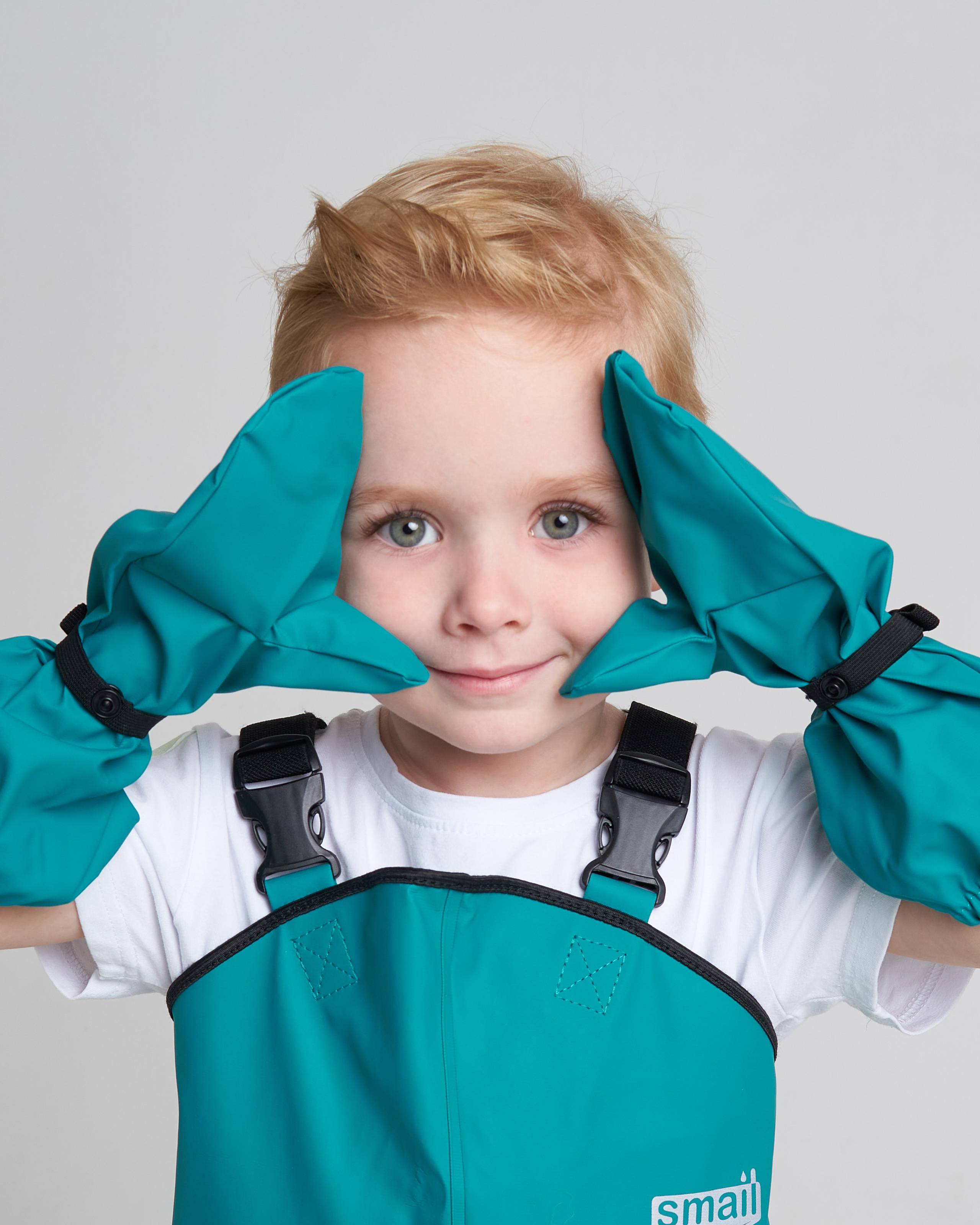 Мальчик в бирюзовых рукавицах держит руки у лица