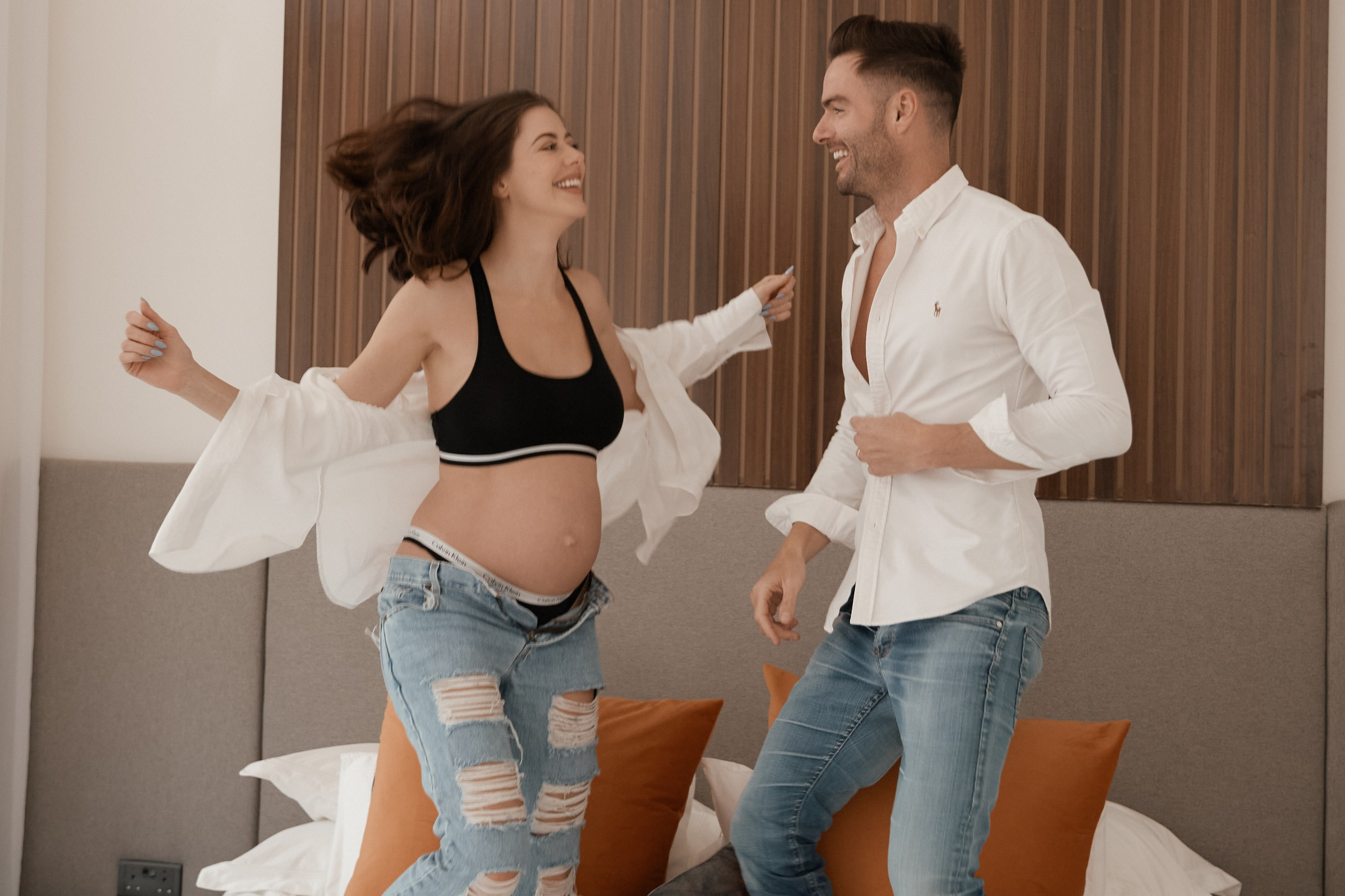 Expectant couple joyfully jumping on a bed during a maternity photoshoot