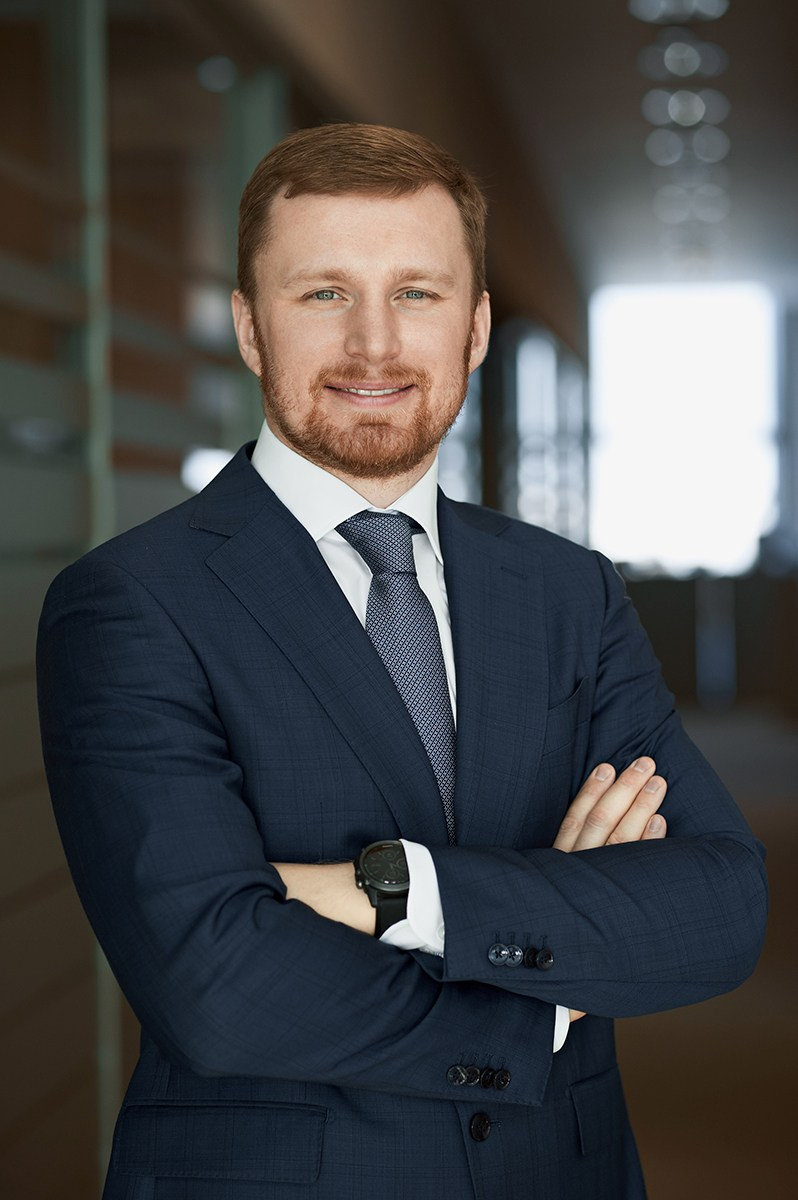 Поясной деловой портрет мужчины, специалиста в офисе, с интерьером и окном на фоне, руки сложены