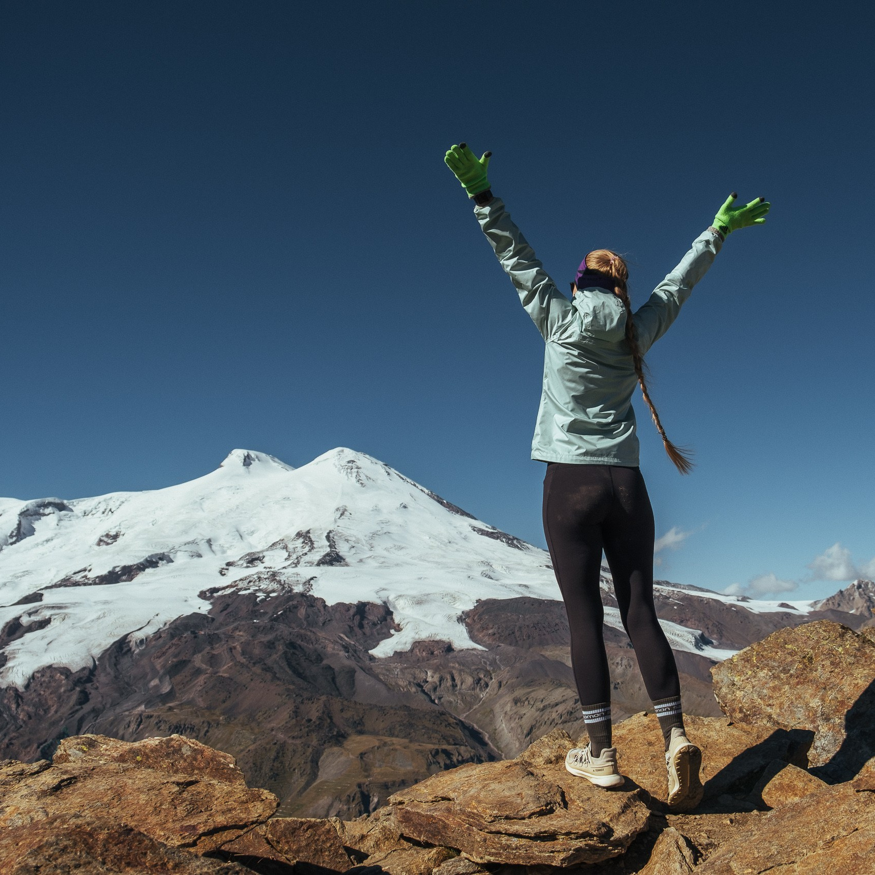 Туристка на горном хребте на фоне Эльбруса, поднятые руки