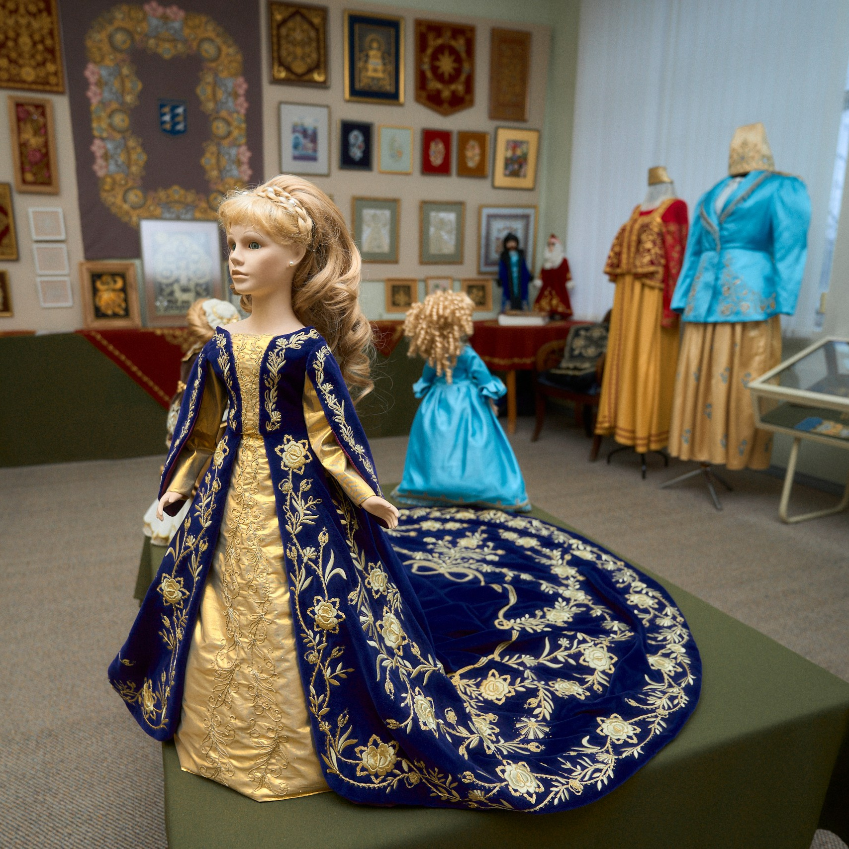 Экспозиция в Музее торжокских золотошвей в Торжке, представляющая манекены в традиционных русских нарядах с золотой вышивкой и сложными узорами, на фоне стен, украшенных картинами и орнаментами