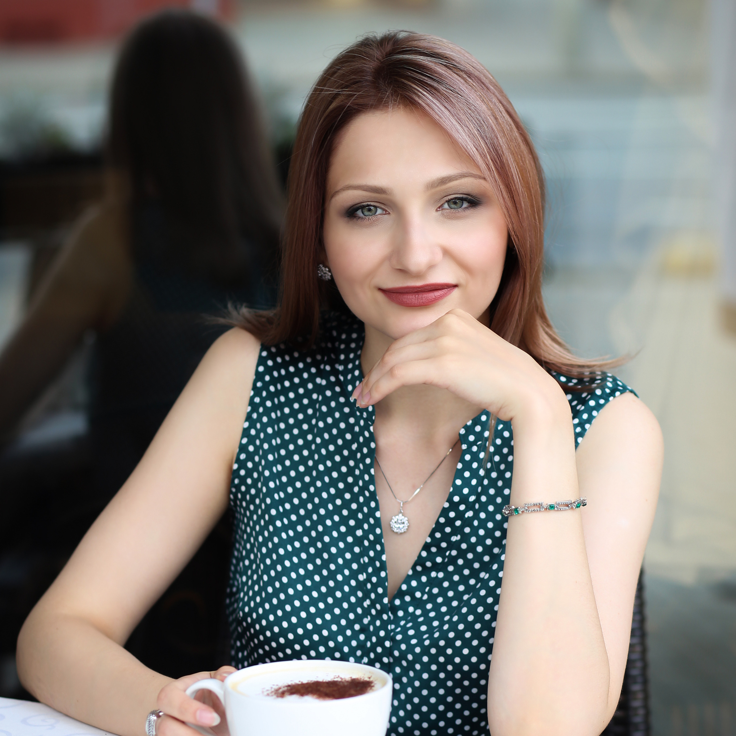 молодая красивая девушка в зеленой блузке пьет кофе в кафе