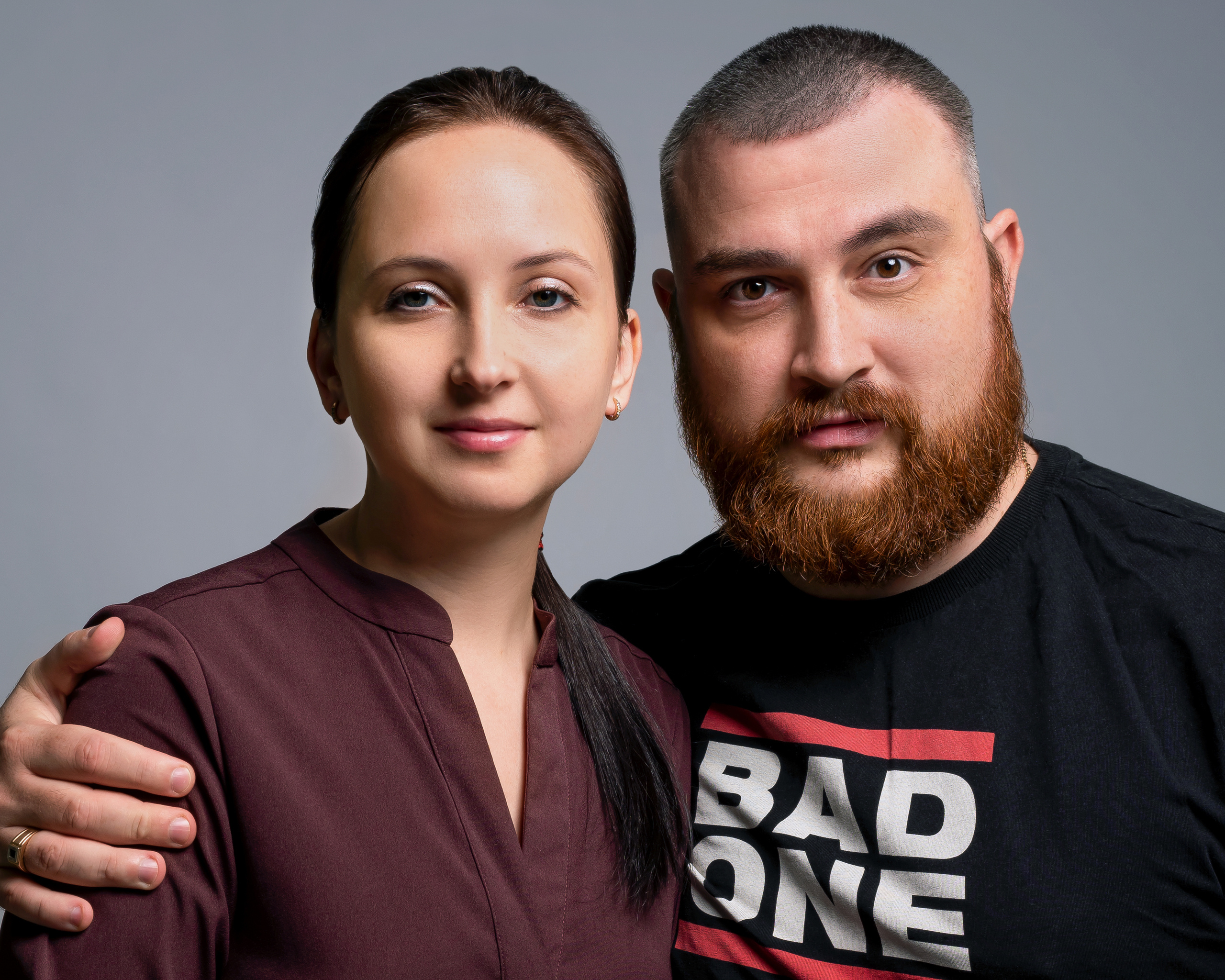 Крупный портрет фотографов, мужчины с рыжей бородой и женщины в бордовой блузке, мужчина обнимает ее за плечо, они смотрят на нас