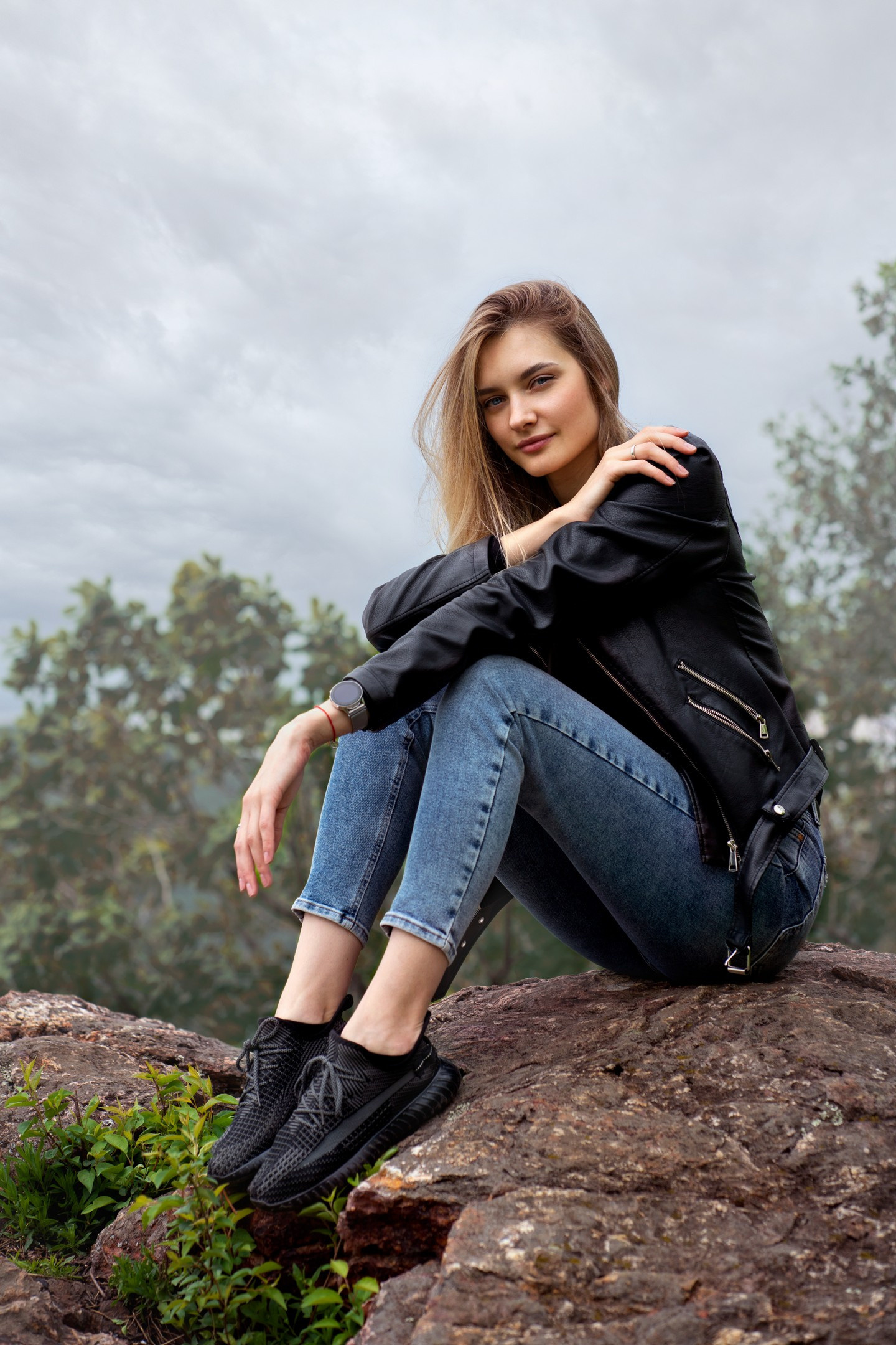 Ростовой портрет девушки в синих джинсах и чёрной кожанной куртке на природе.