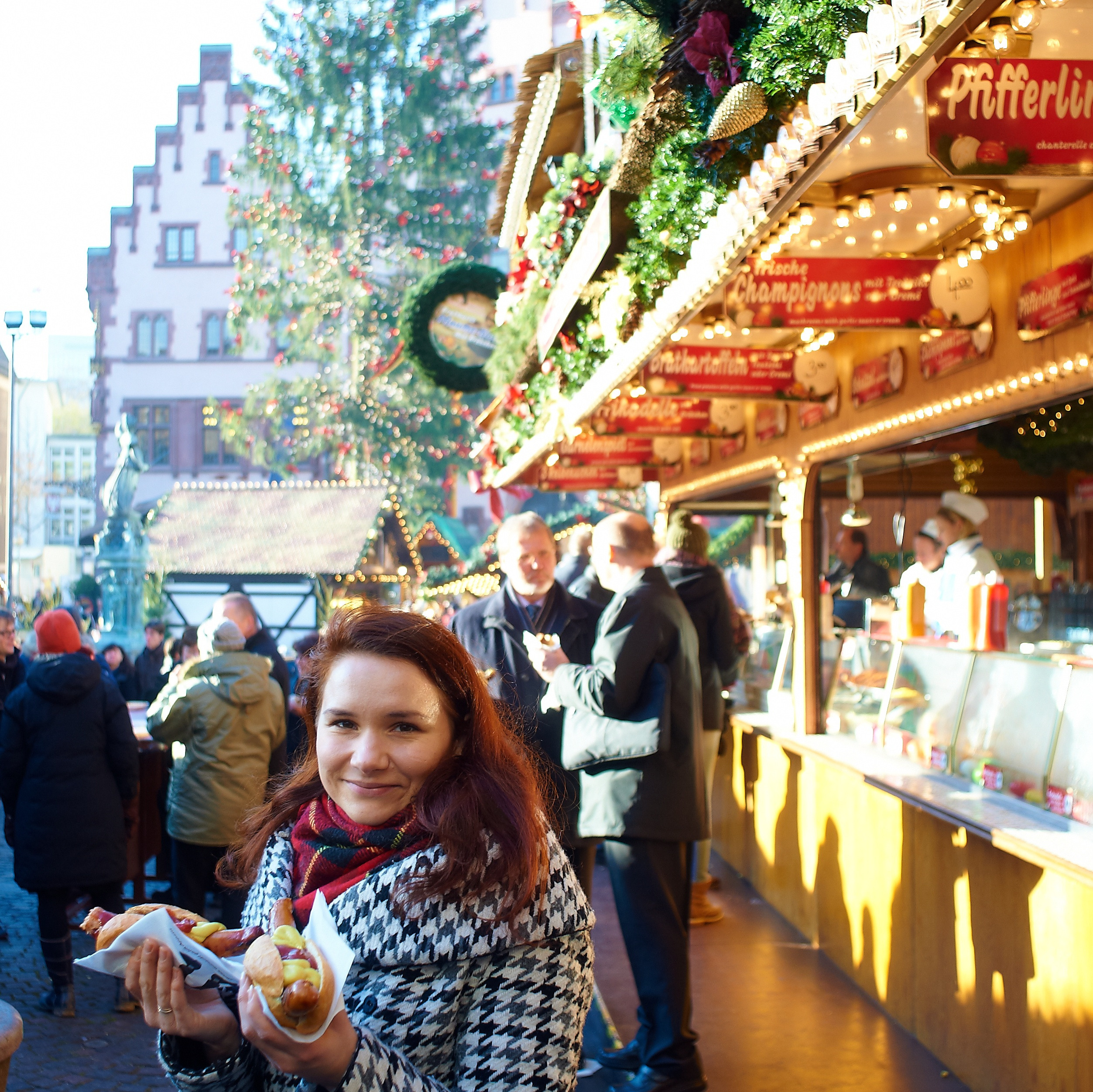 Рождественский рынок в Германии, девушка держит сосиски, новогодняя елка, рождественские угощения