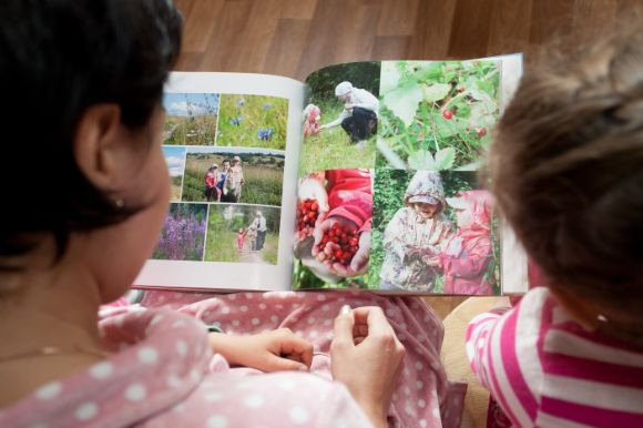 Женщина и девочка смотрят семейную фотокнигу, держа ее у себя на коленках.