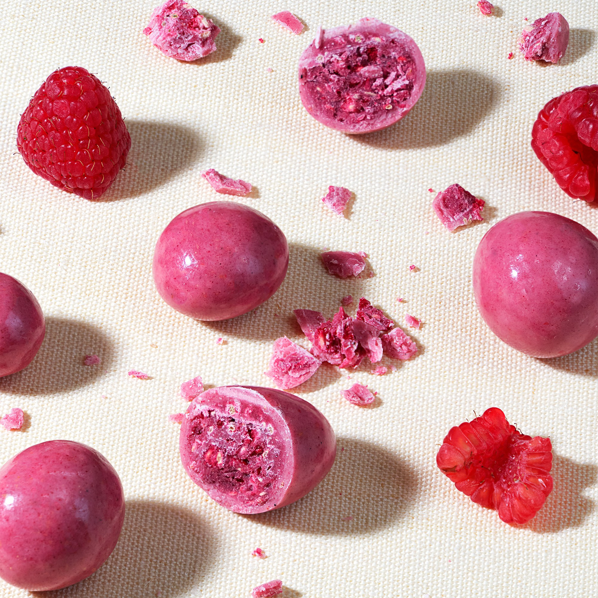 Много конфет из малины и розового шоклада на бежевой скатерти