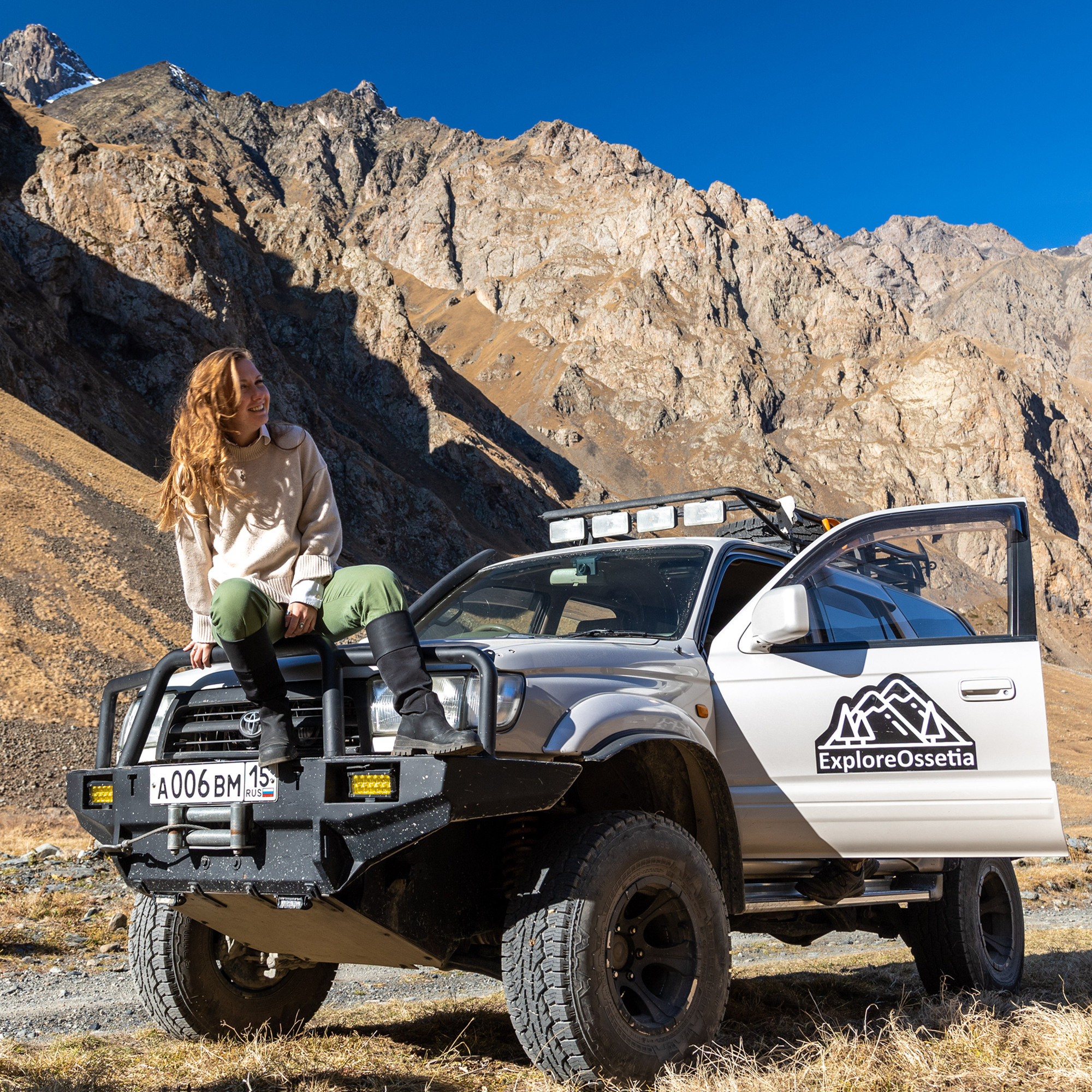 Девушка сидит на капоте внедорожника тойота Hilux SURF на фоне гор, сборный джип тур по горам Осетии