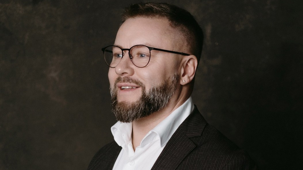 симпатичный мужчина в белой рубашке с бородой улыбается и в руках держит фотокамеру. Фотограф Денис Ожигин Краснодар, пос.&nbsp;Южный (Динской район) с&nbsp;выездом по&nbsp;Краснодару и&nbsp;Краснодарскому краю