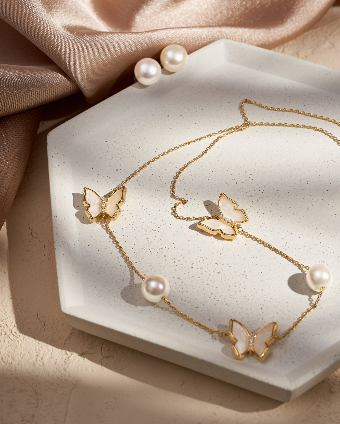 Позолоченное колье с бабочками из перламутра и жемчужинами лежит на бетонной подставке