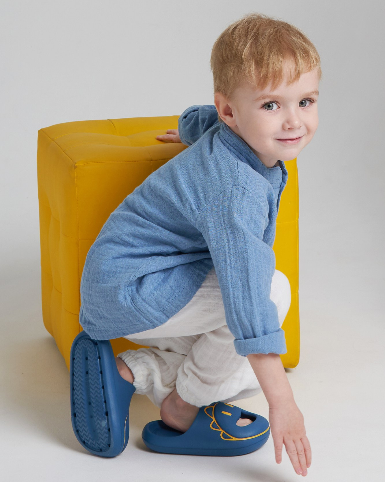 Ребенок модель в голубой рубашке присел на фоне желтого куба
