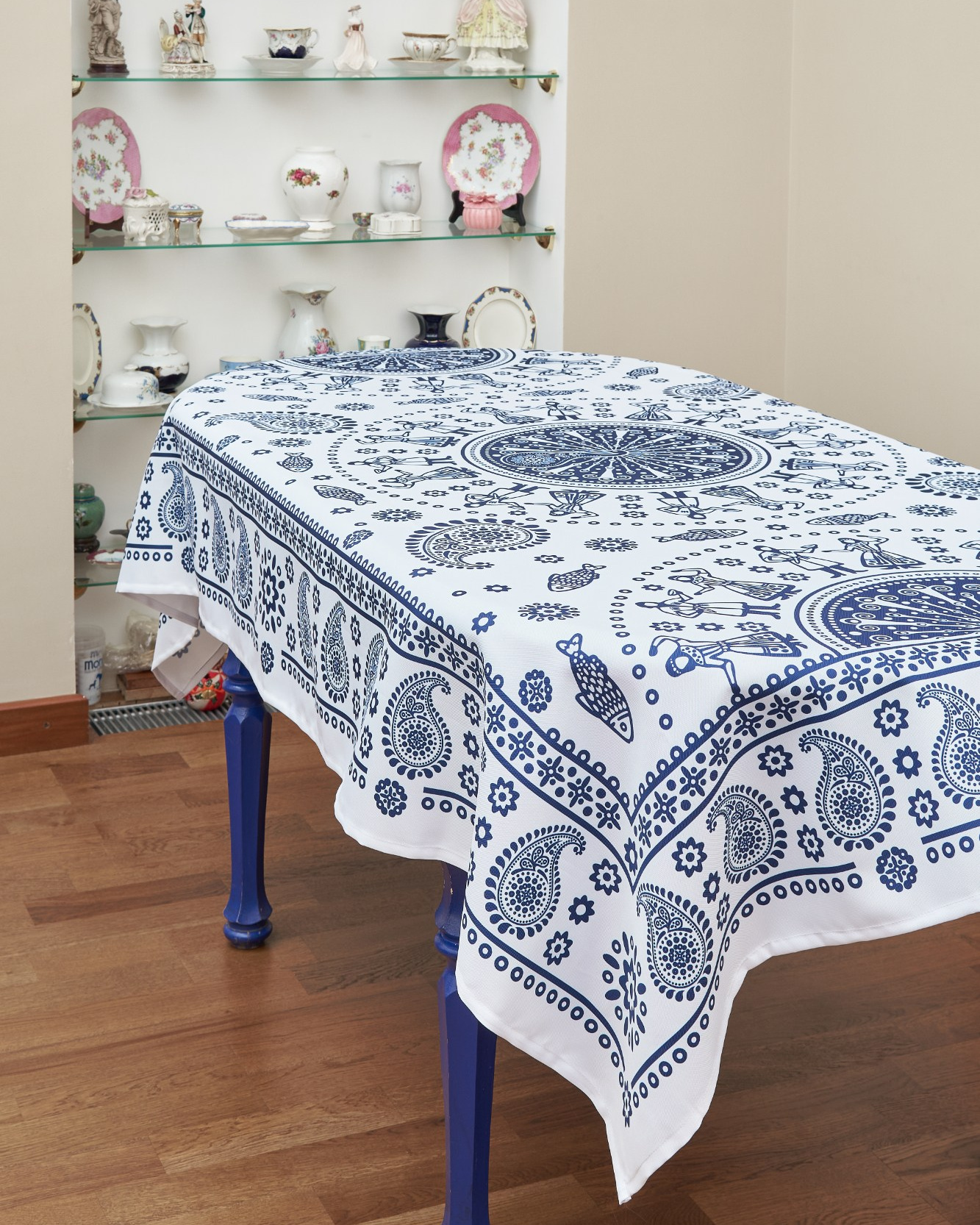 Белая с синим скатерть лежит на столе который стоит на деревянном полу