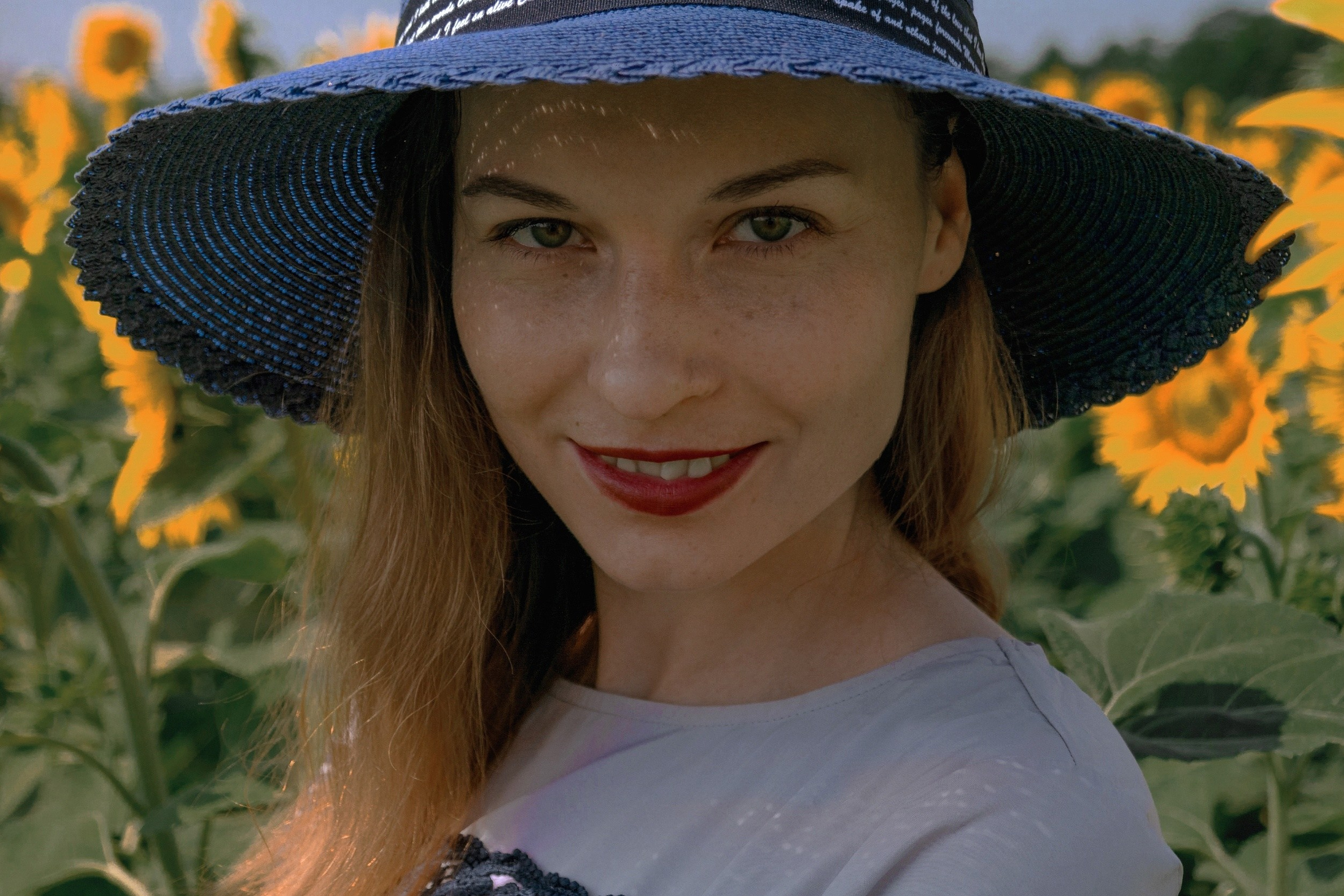 девушка улыбается на фоне подсолнухов, на девушке синяя шляпа