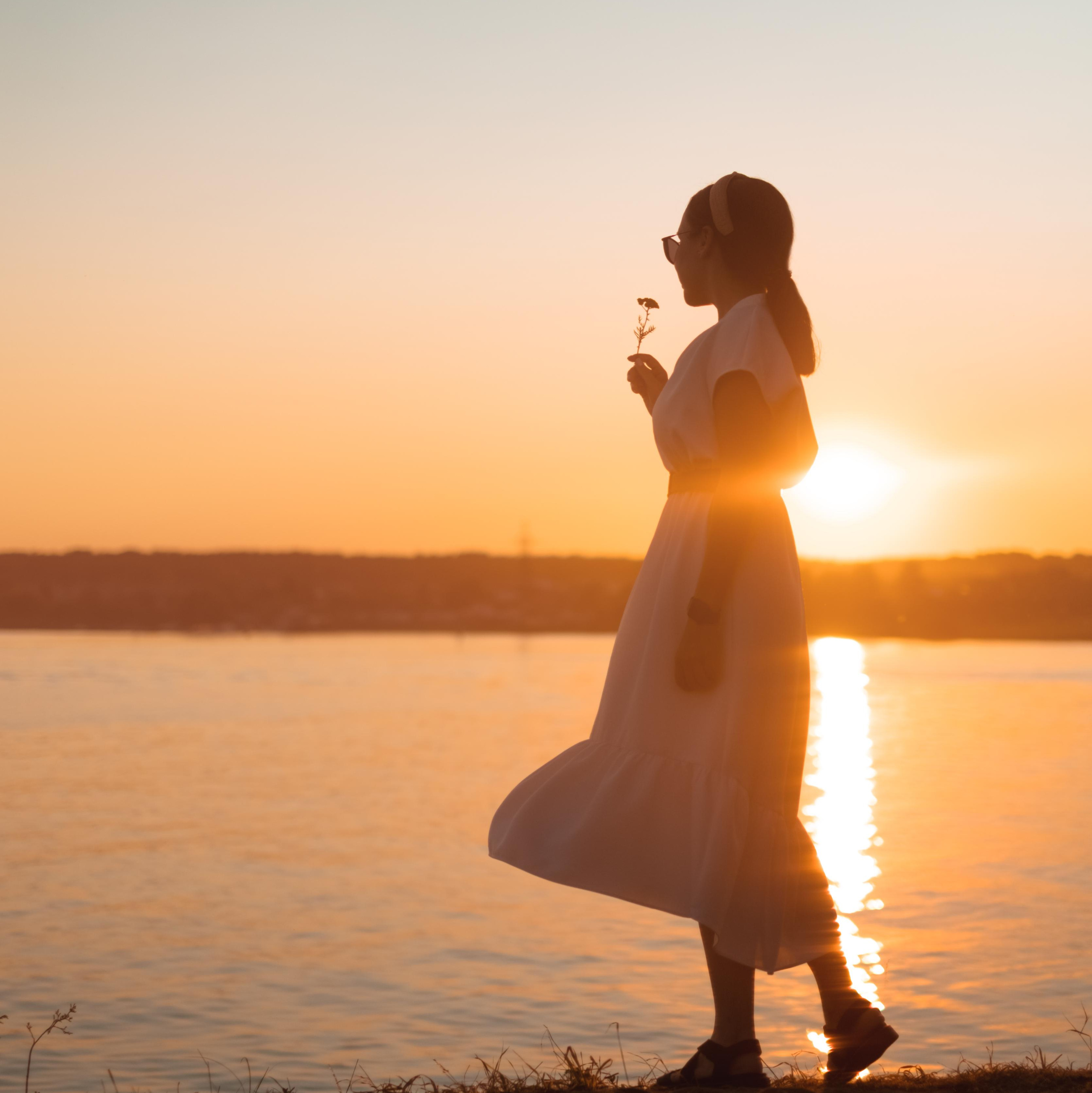 Девушка на фоне заката на берегу реки в белом платье 