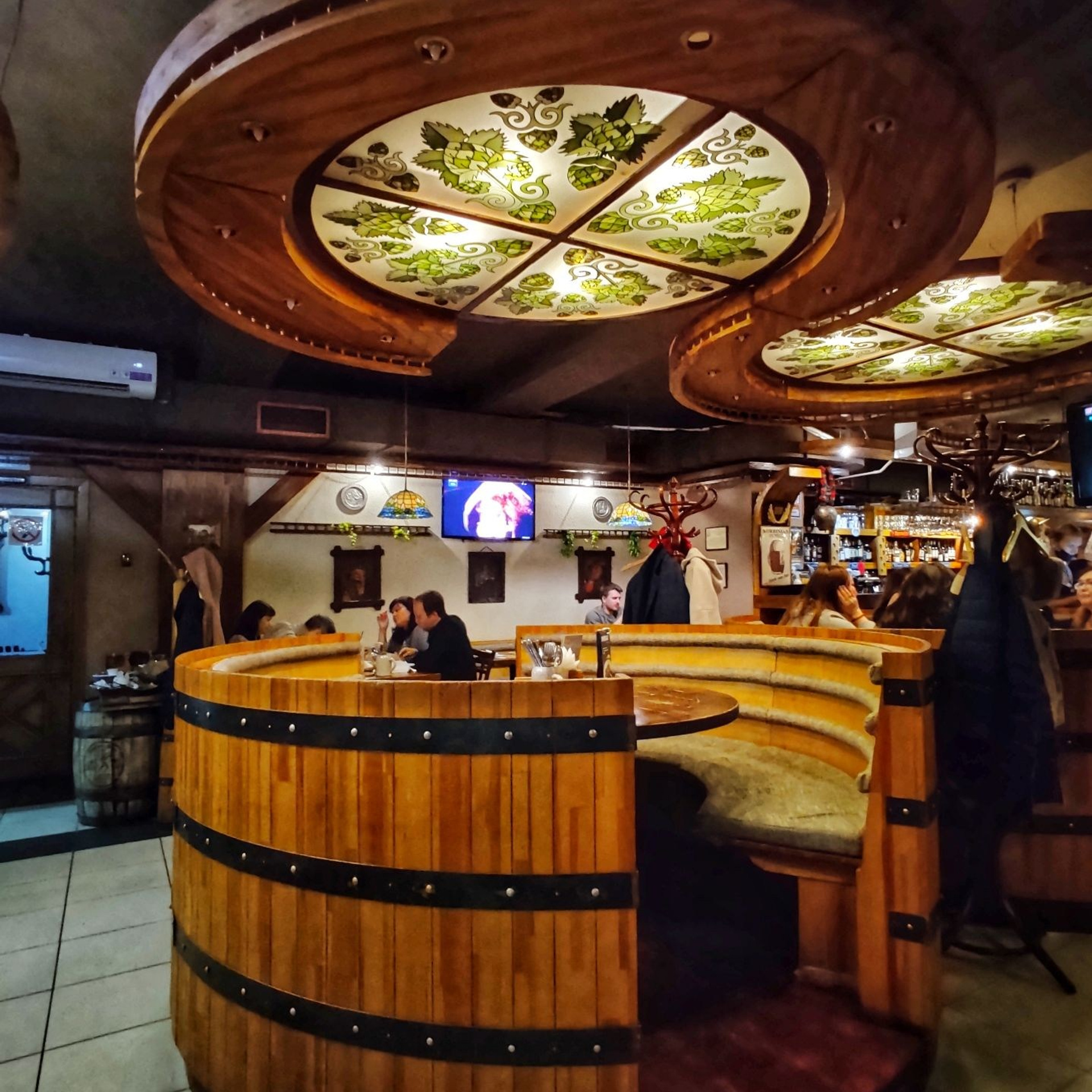 Круглая деревянная кабина в виде пивной бочки с мягкими сиденьями в интерьере пивного бара