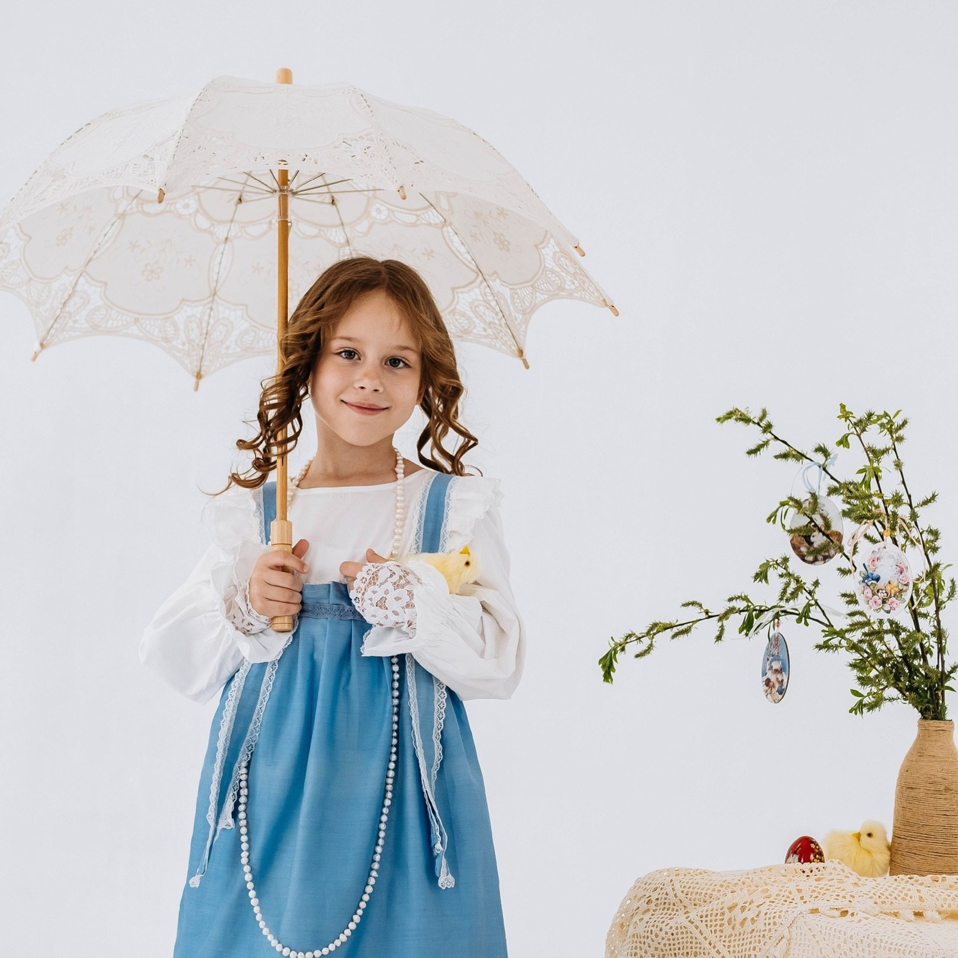 Винтажный кружевной зонтик держит девочка в сарафане. Студийная детская фотосессия. 