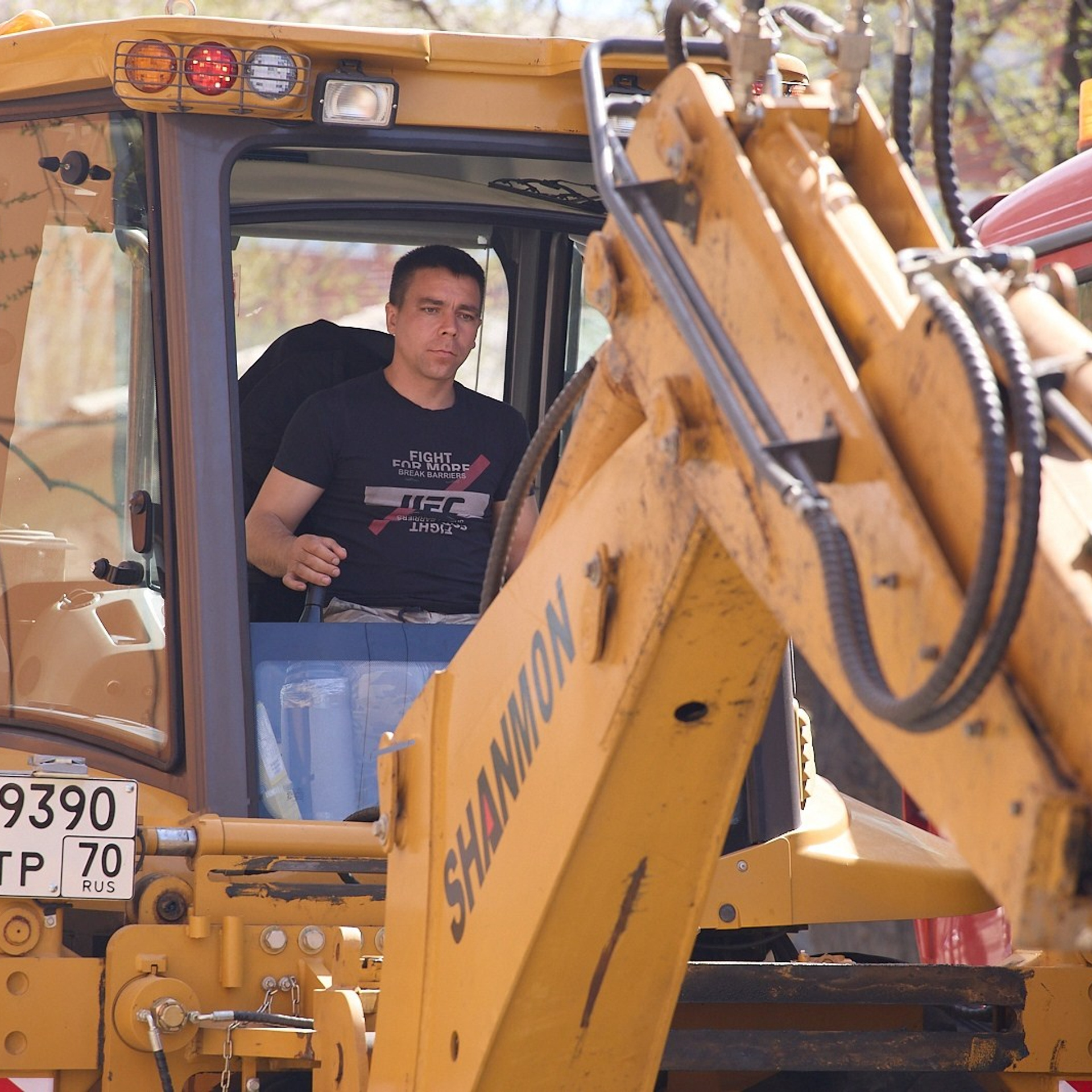 Молодой тракторист-экскаваторщик в кабине управляет жёлтым экскаватором, очень сосредоточен Улица Фрунзе, Томск.