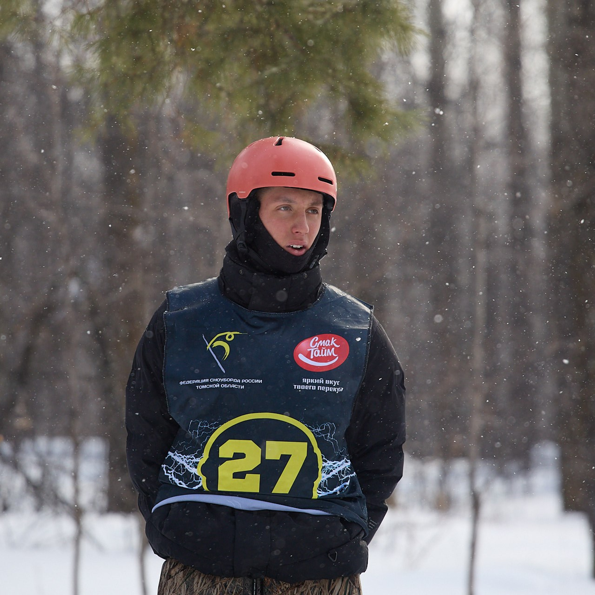 Сноубордист в оранжевом шлеме на фоне леса.