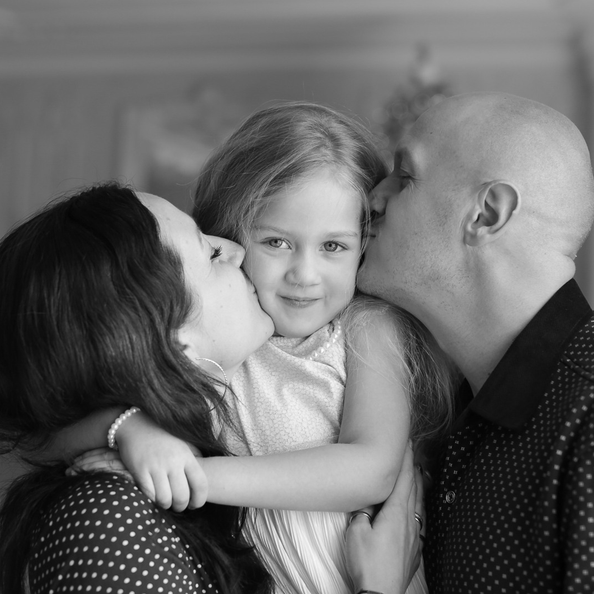 Семейная фотосессия, Девочка на руках у мамы, и папа с мамой целуют ее в обе щеки