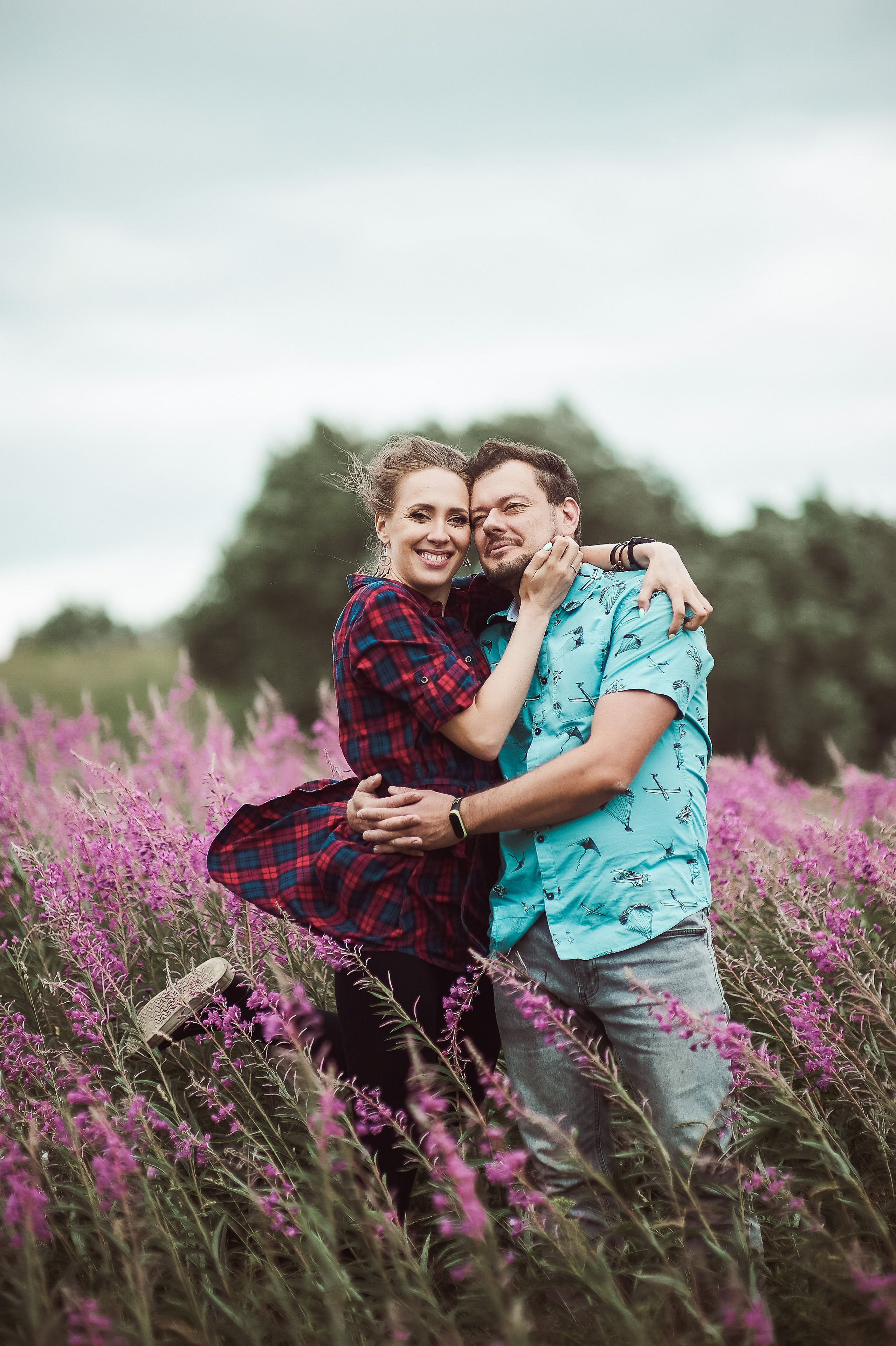 Ветренная фотосессия Love story в пригороде Петербурга, где двое влюблённых стоят и прижимают нежно друг друга, в поле с иван-чаем. 