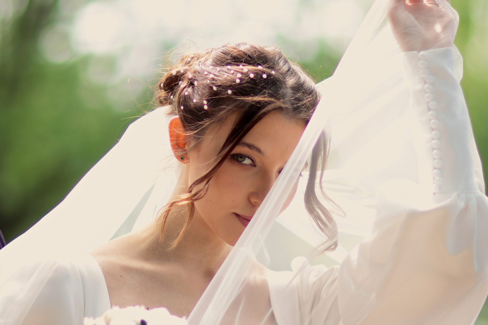 Невеста русоволосая девушка закрывает часть лица фатой.