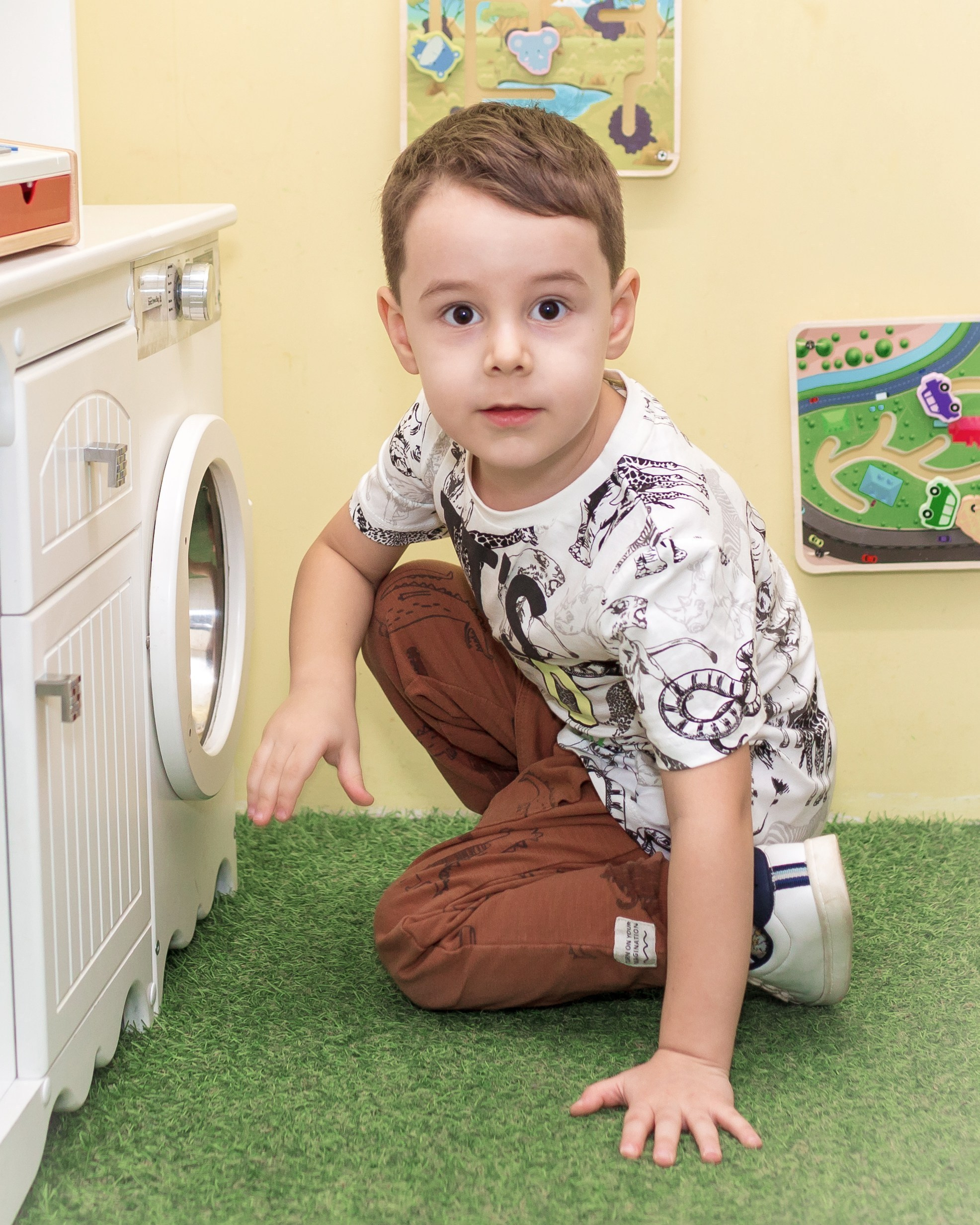 Мальчик сидит на полу перед игрушечной стиральной машиной