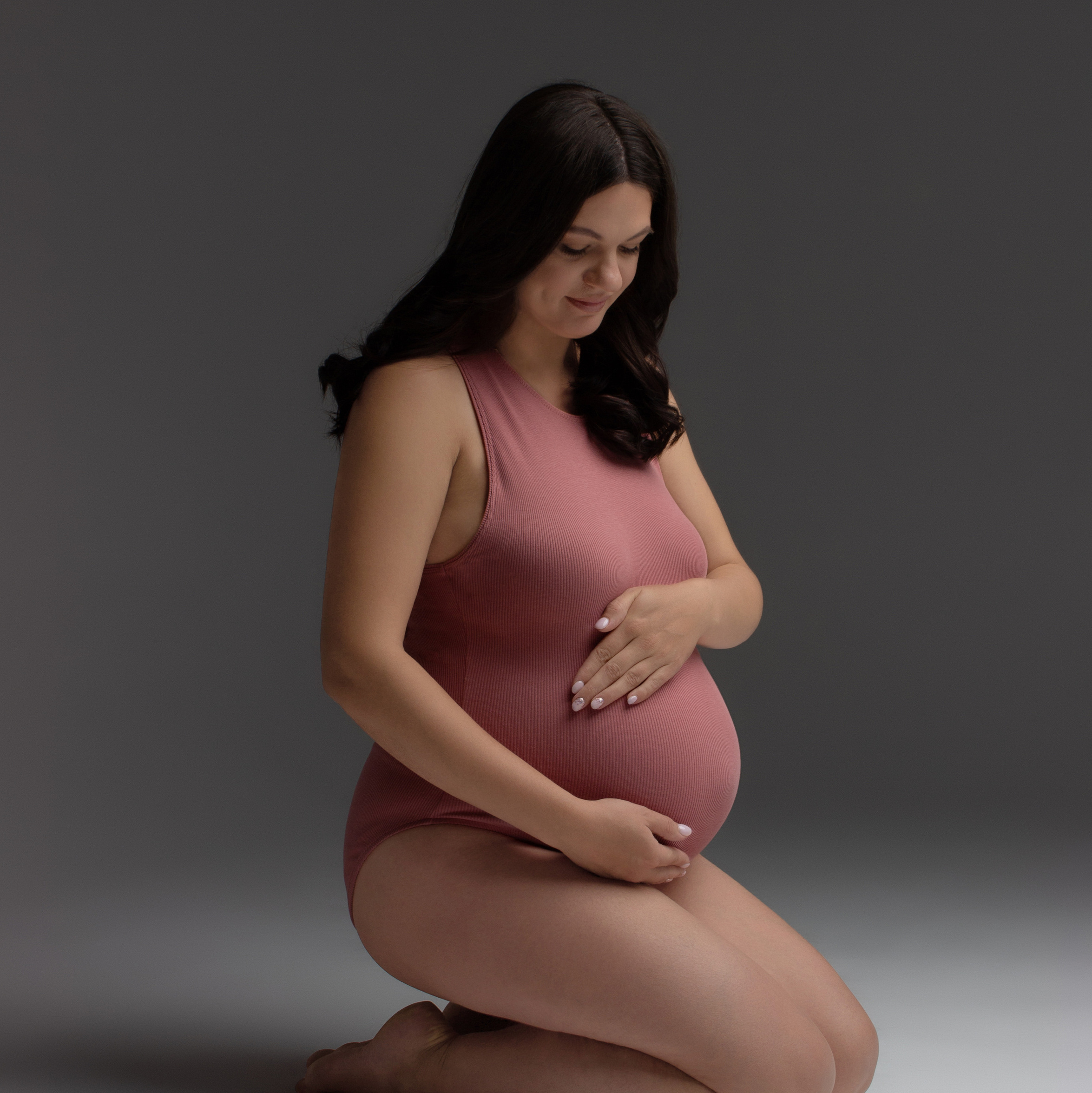беременная девушка в розовом боди сидит на коленях
