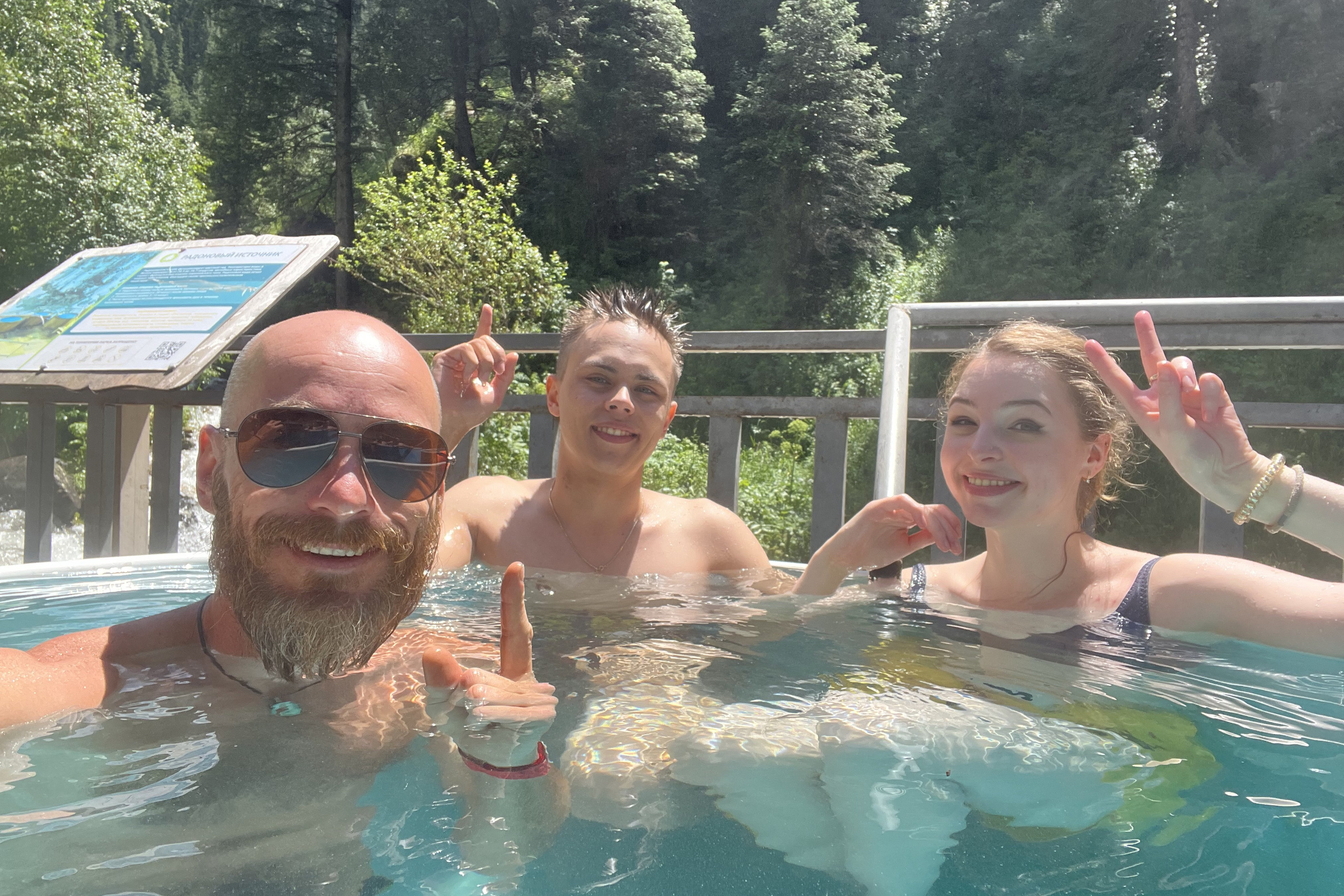 Величественный Чарынский каньон в районе Алматы с ярко-красными скалами, пересечённый извилистой дорогой, на которую падают длинные вечерние тени. Захватывающее сочетание красочных утёсов, зелёных склонов и драматичного неба создаёт эффектный пейзаж