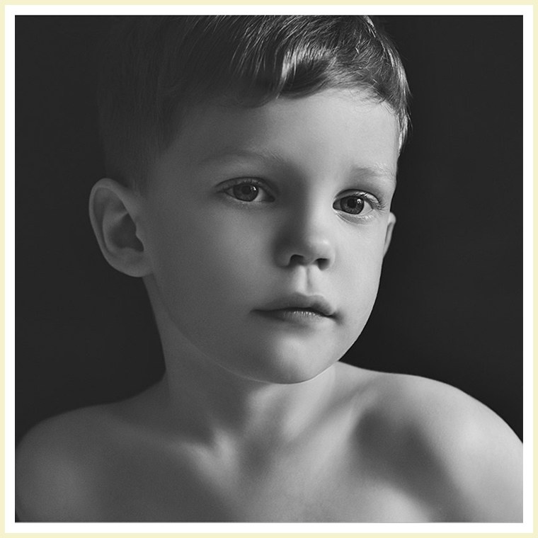 Детская фотосъемка дома - портрет мальчика без рубашки на тёмном фоне.