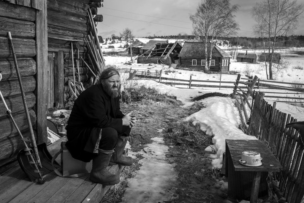 Father Arkady is sitting on the porch of a rural house and basking in the spring sun. Spring 2017.