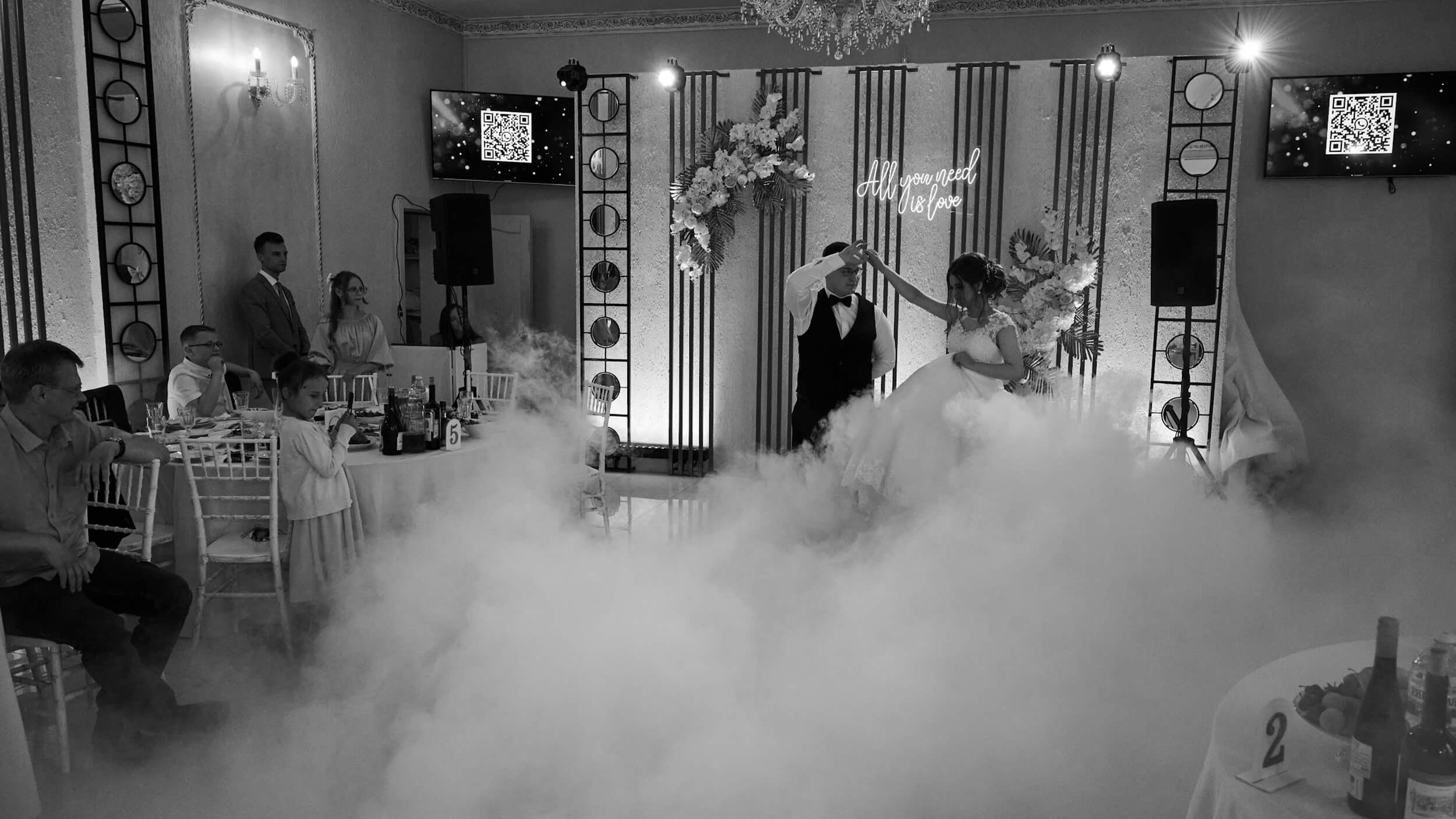 Пара кружится в первом свадебном танце в банкетном зале. Мягкий свет софитов, тяжелый дым. Кадр передаёт радость и торжественность момента.